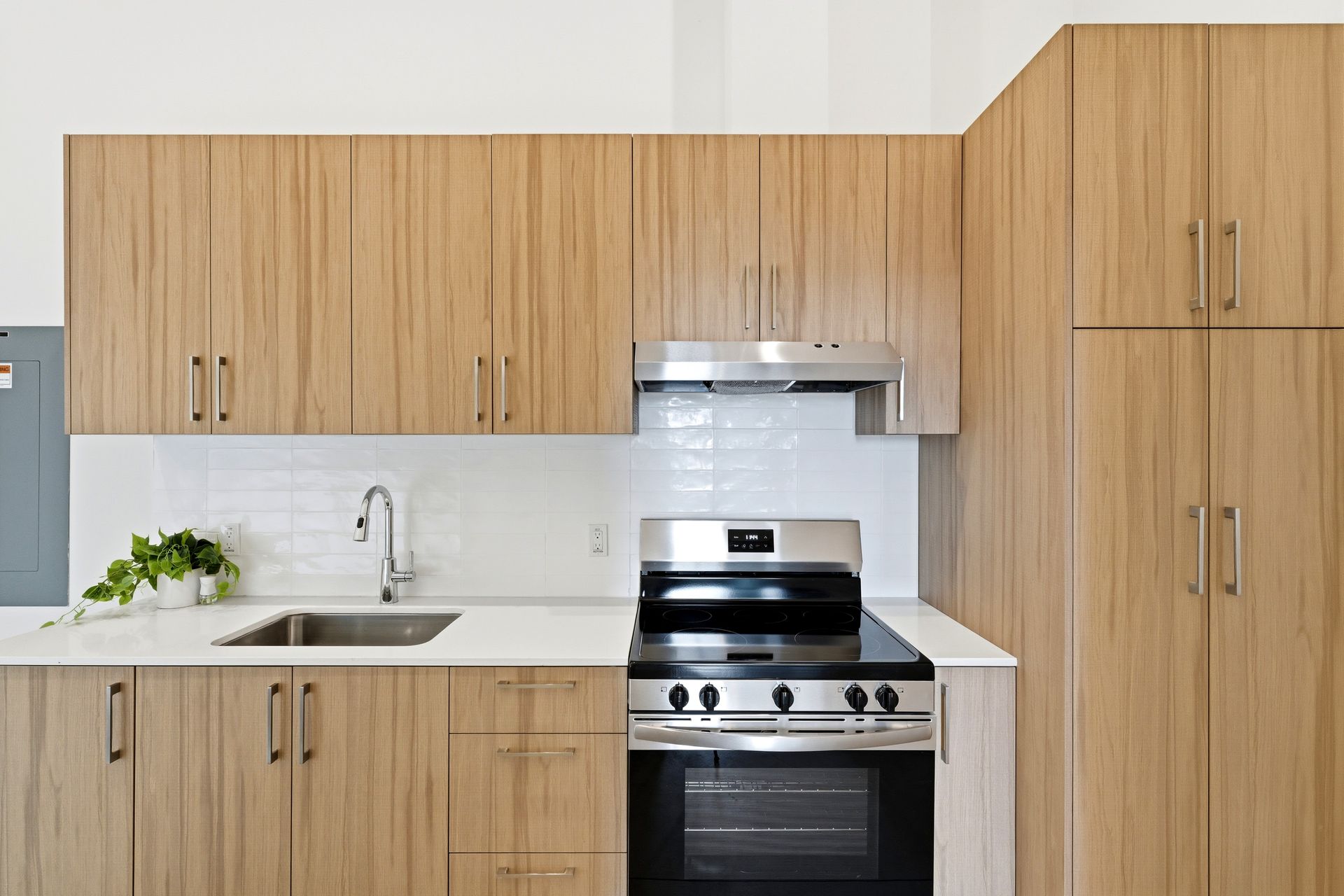Modern kitchen with light wood cabinets, stainless steel stove, sink, and white countertops