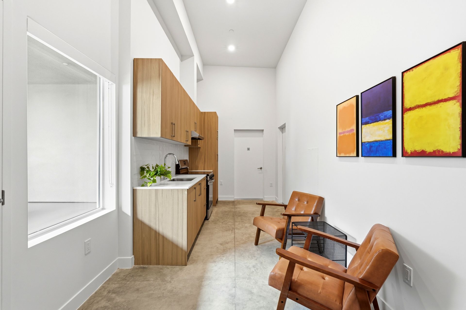 Bright hallway with kitchenette, two wooden chairs, and colorful wall art.