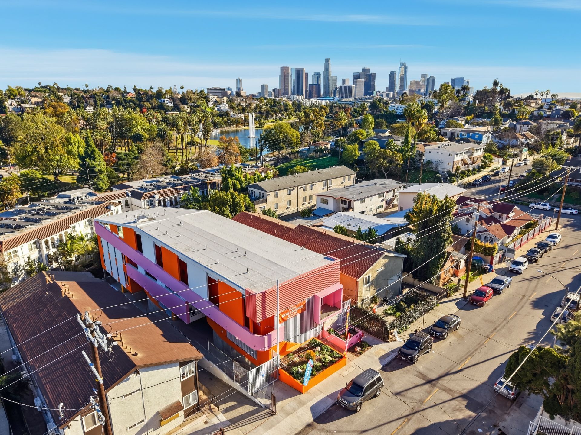 Colorful building with LA skyline in the background. Pink, orange, and white facade. Cars line street.