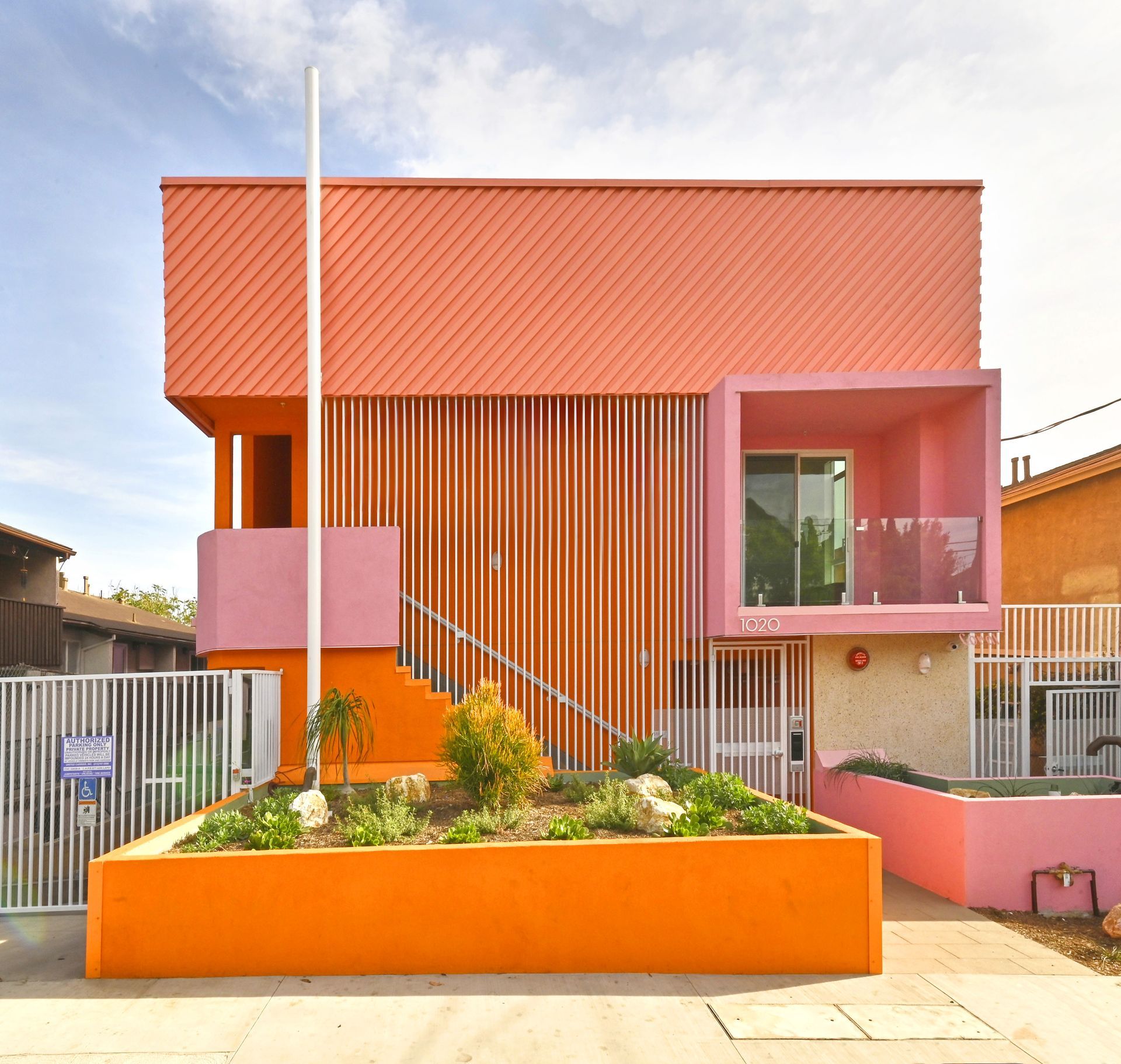 Brightly colored modern building with salmon and orange facade, wooden slats, and raised garden bed.