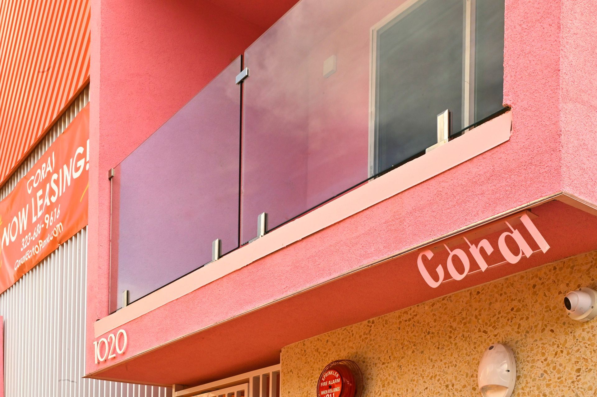 Coral-colored building with glass balcony, a sign that says 