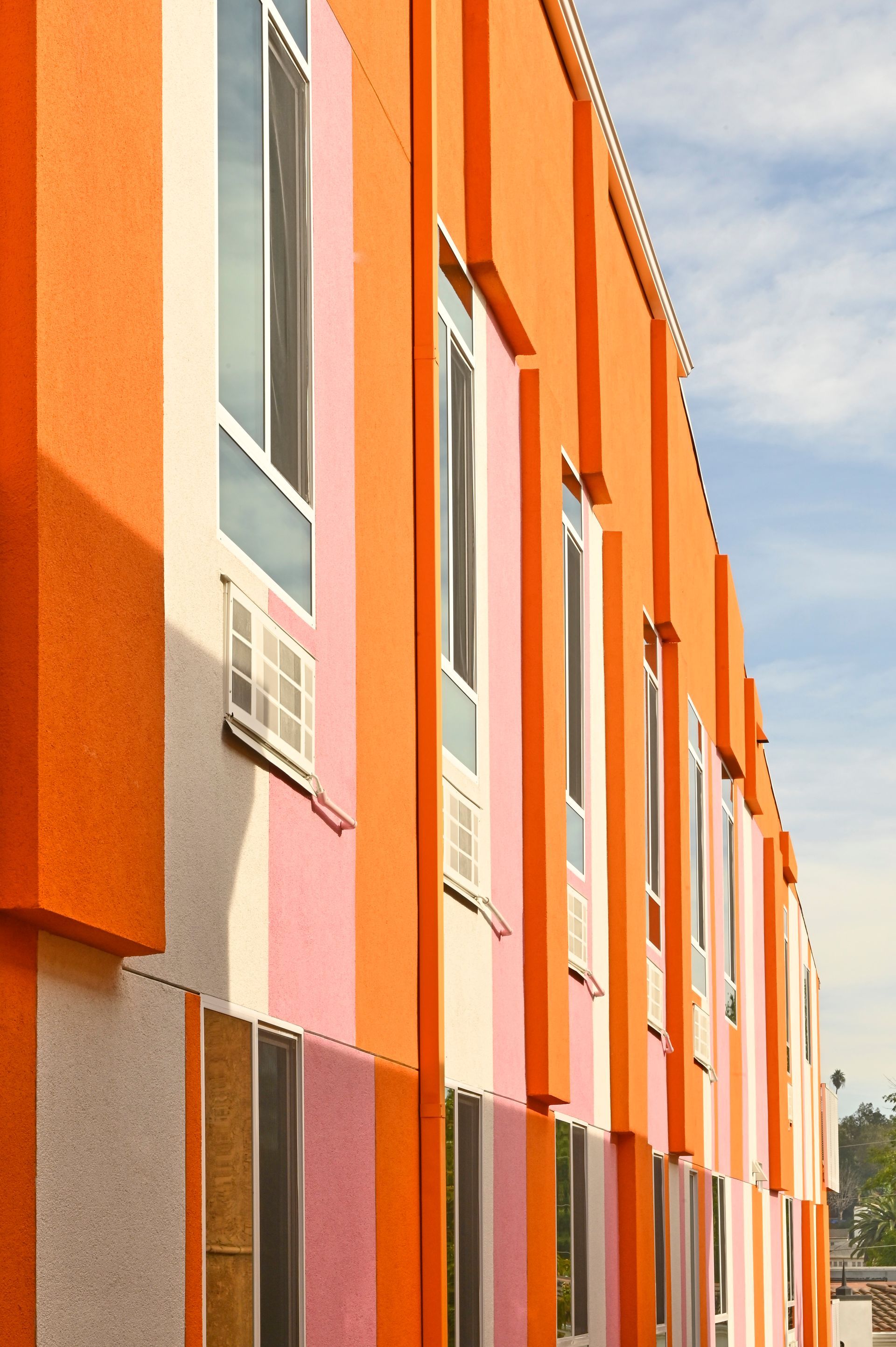 Orange and pink striped building with rectangular windows under a blue sky.
