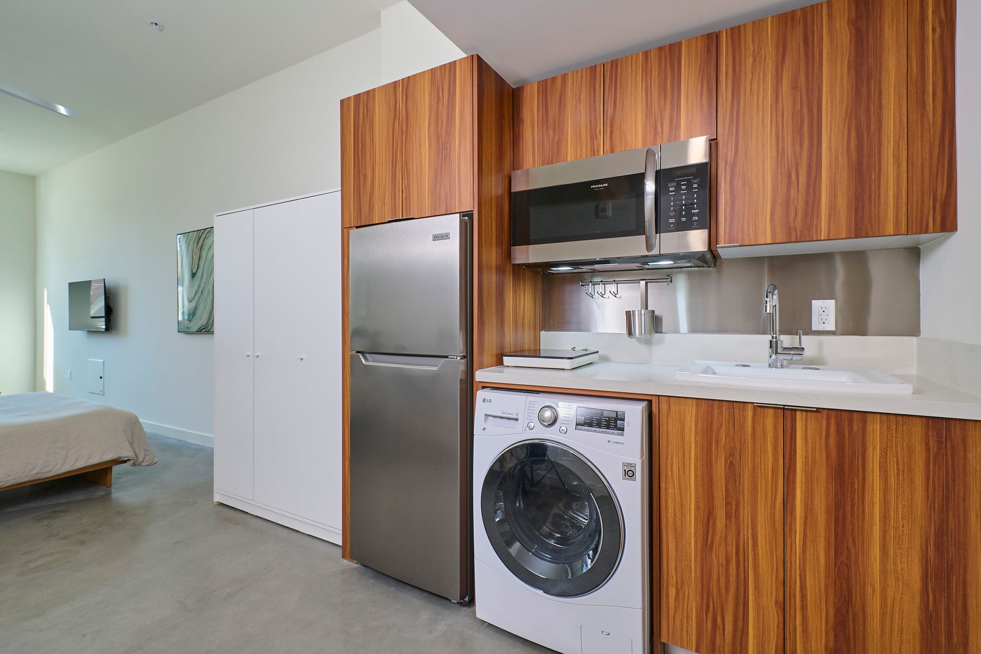 A kitchen with a washing machine , refrigerator , microwave and sink.