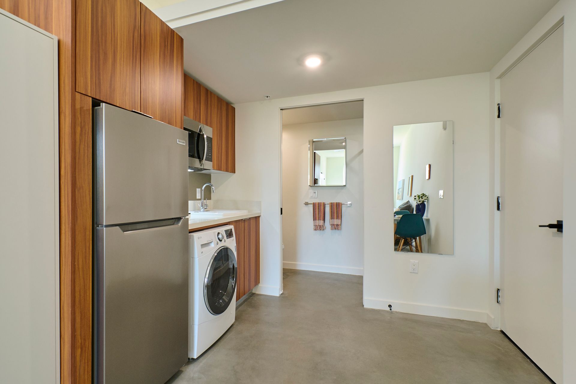 A kitchen with a refrigerator , washer and dryer , and a mirror.