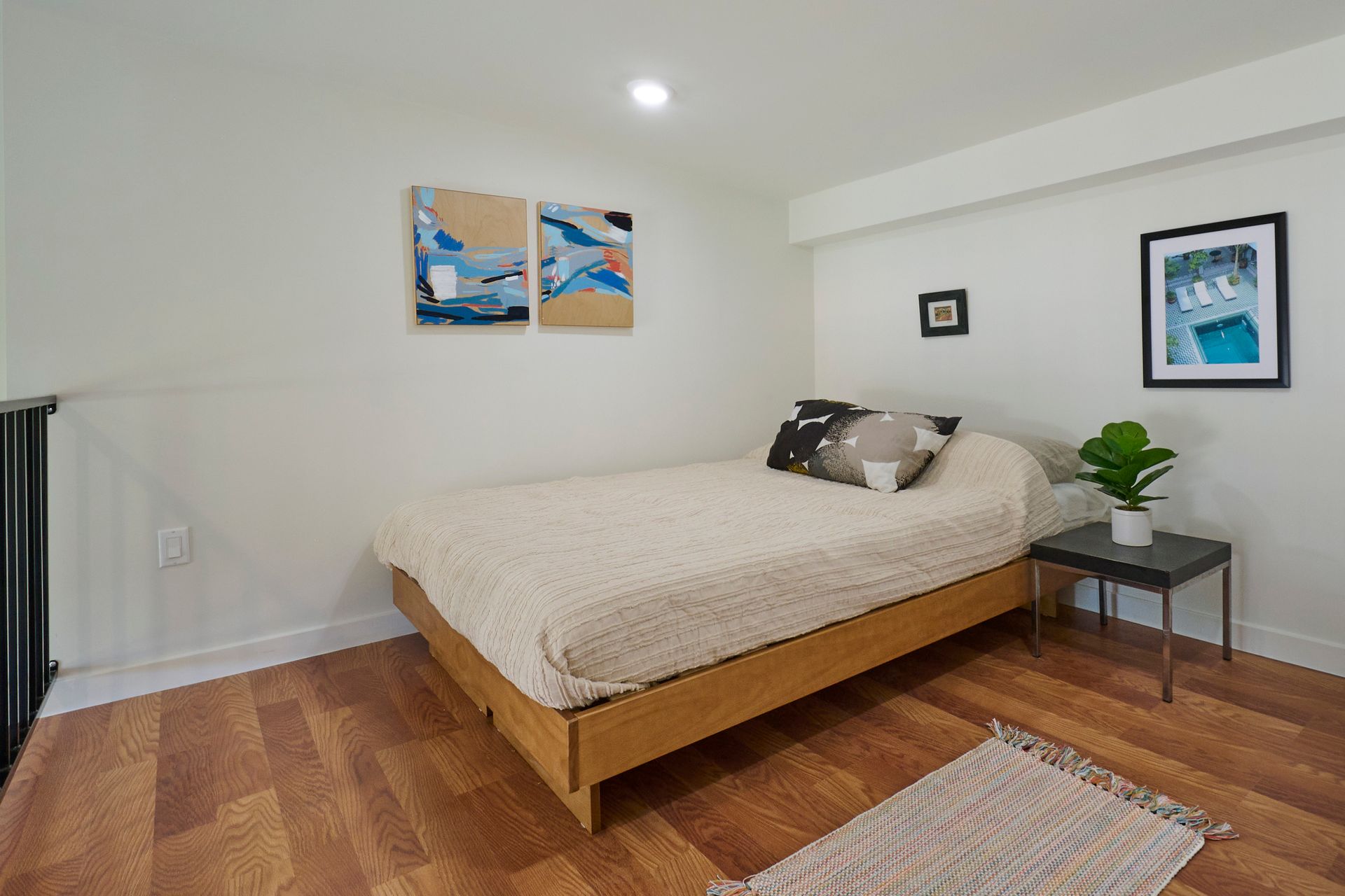 A bedroom with a bed , table , rug and paintings on the wall.