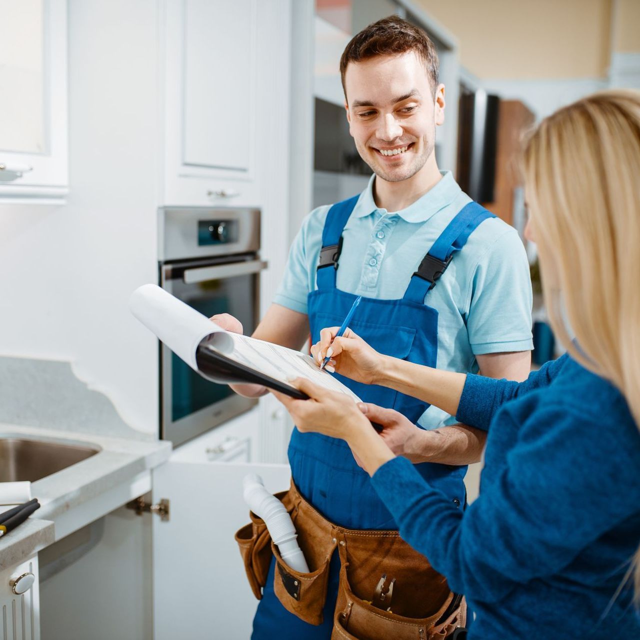 A man in blue overalls is talking to a woman in a kitchen