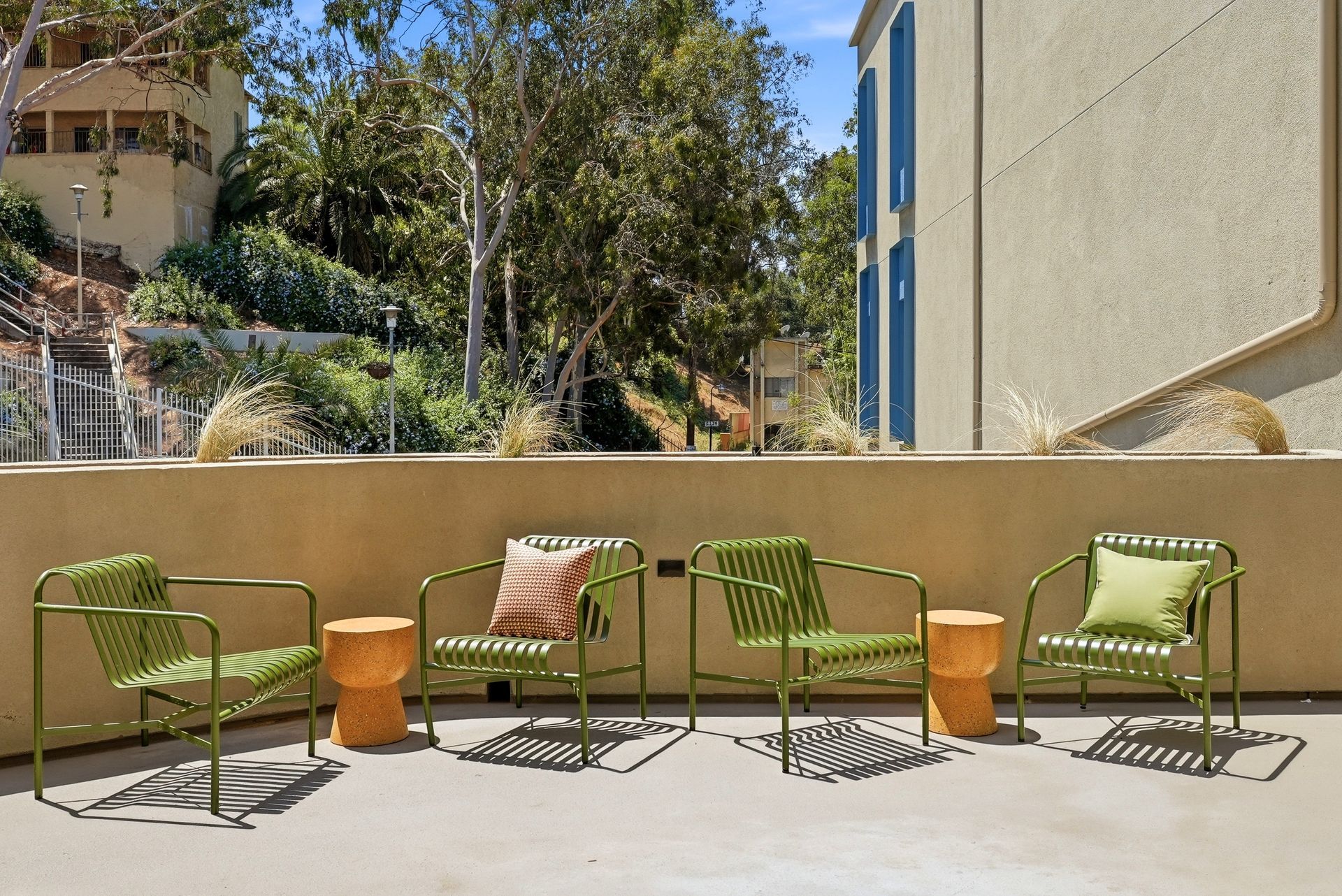 Outdoor patio with four green chairs and a small table against a beige wall in bright sunlight