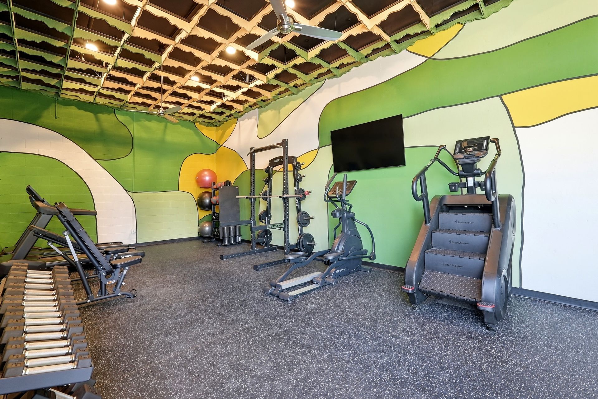 Small gym with weight machines, treadmill, and a mirrored wall in a green and white room.