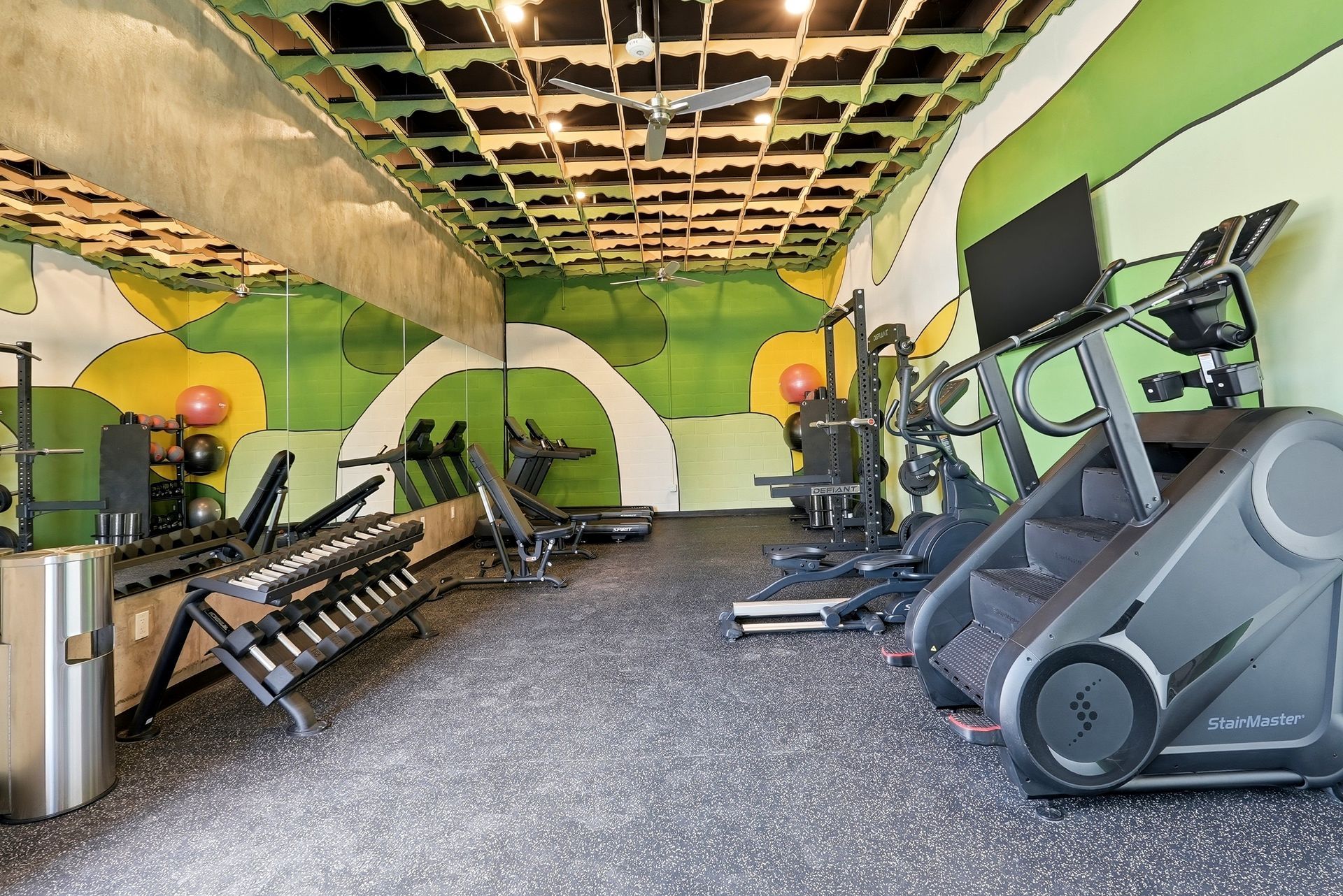 Empty gym with treadmills, weights, and exercise machines in a green and yellow room with a damaged ceiling.