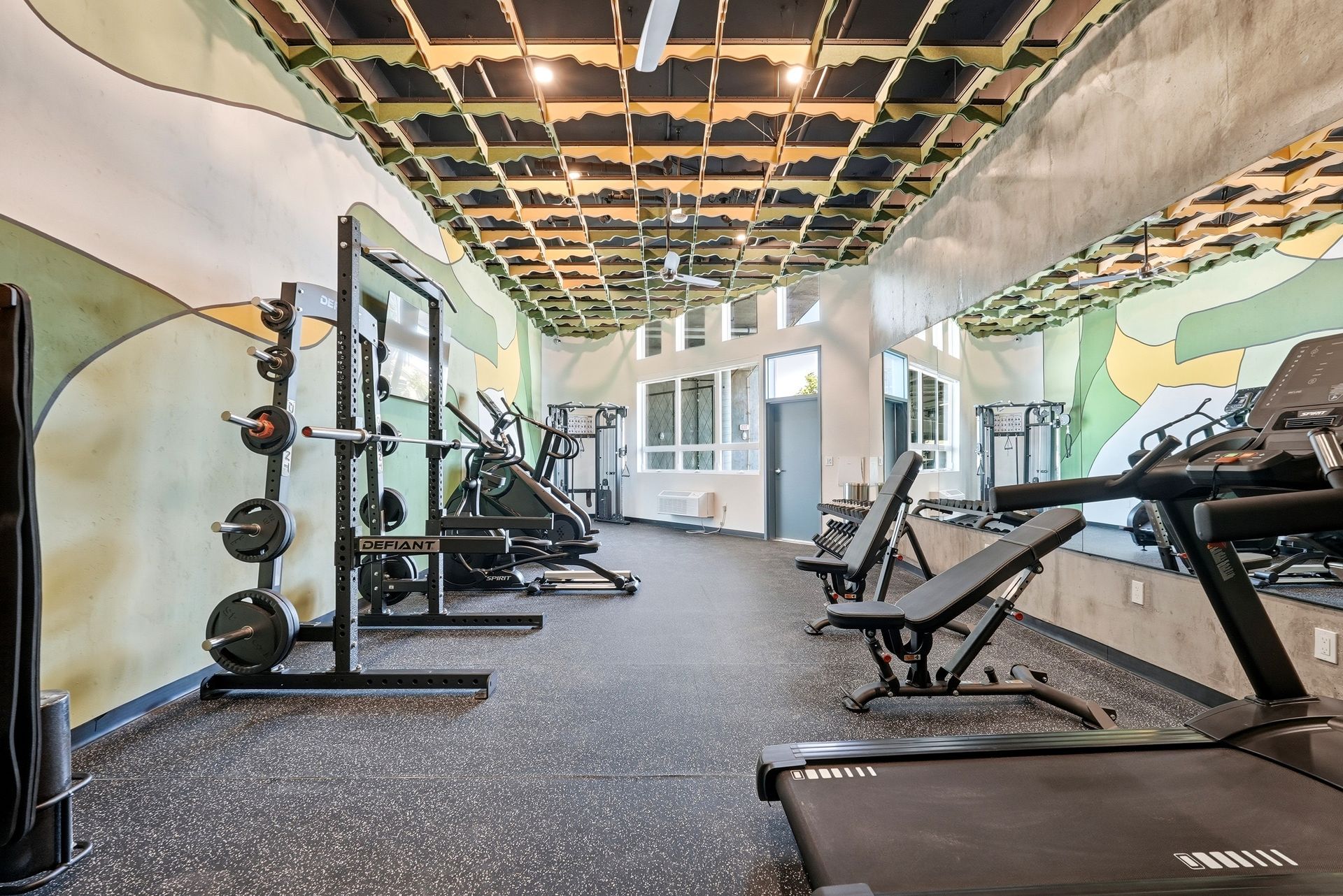 Empty gym with exercise machines, rubber flooring, and exposed ceiling lights.