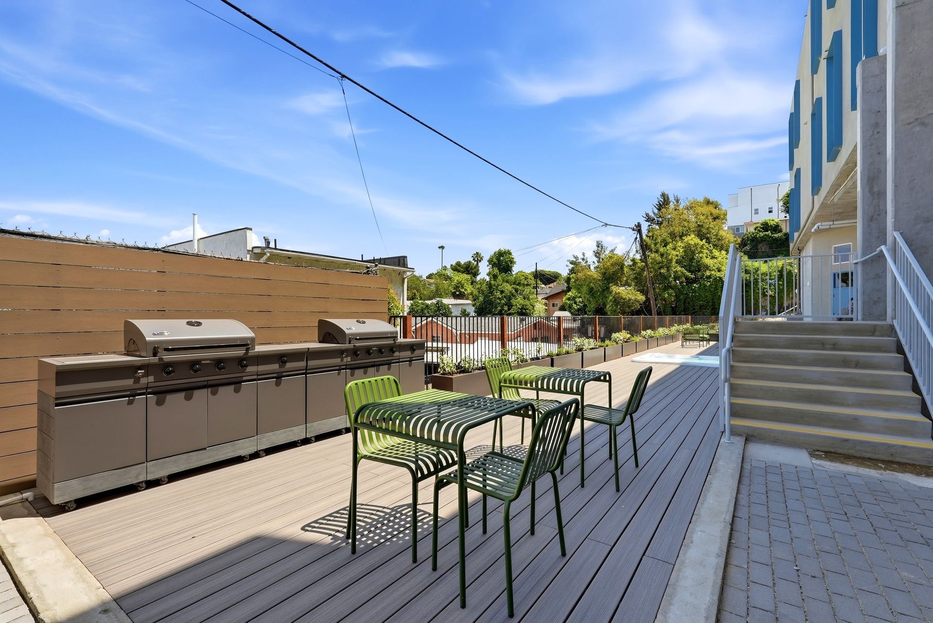 Outdoor deck patio with grill, table and chairs beside stairs on a sunny day