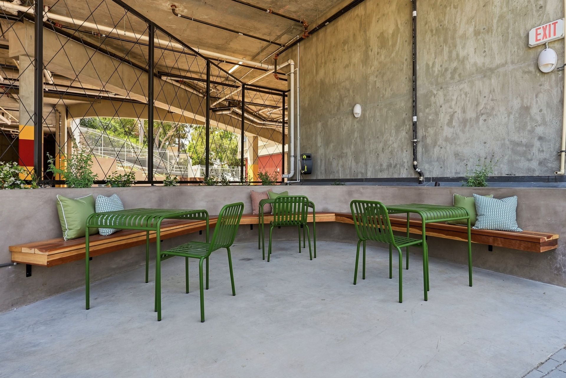 Outdoor patio seating with green metal tables and benches under a covered concrete awning