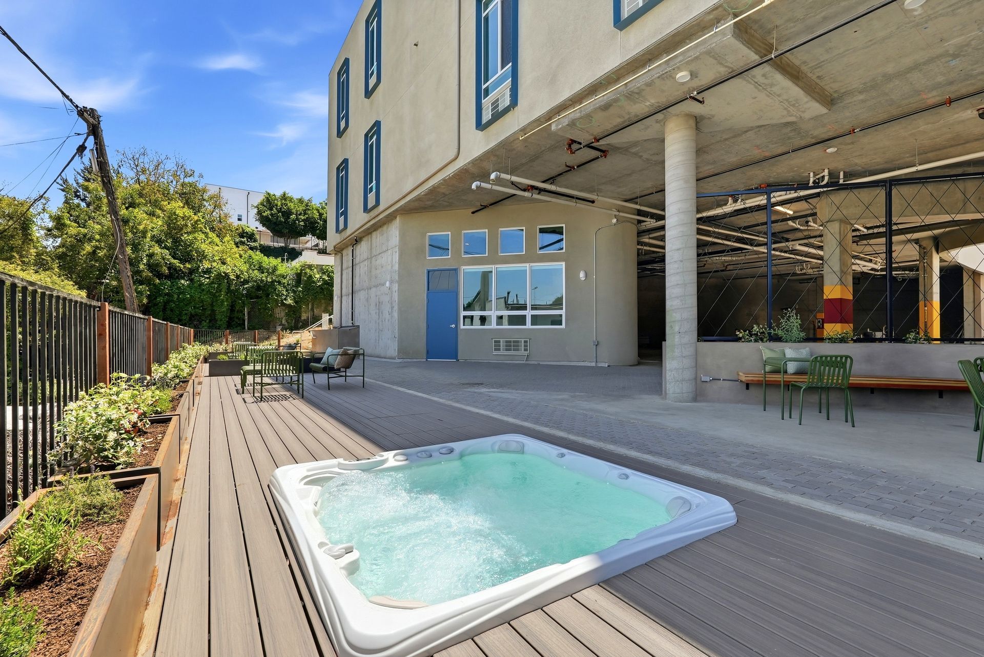 Modern building patio with a small square hot tub, wooden deck, and covered seating area