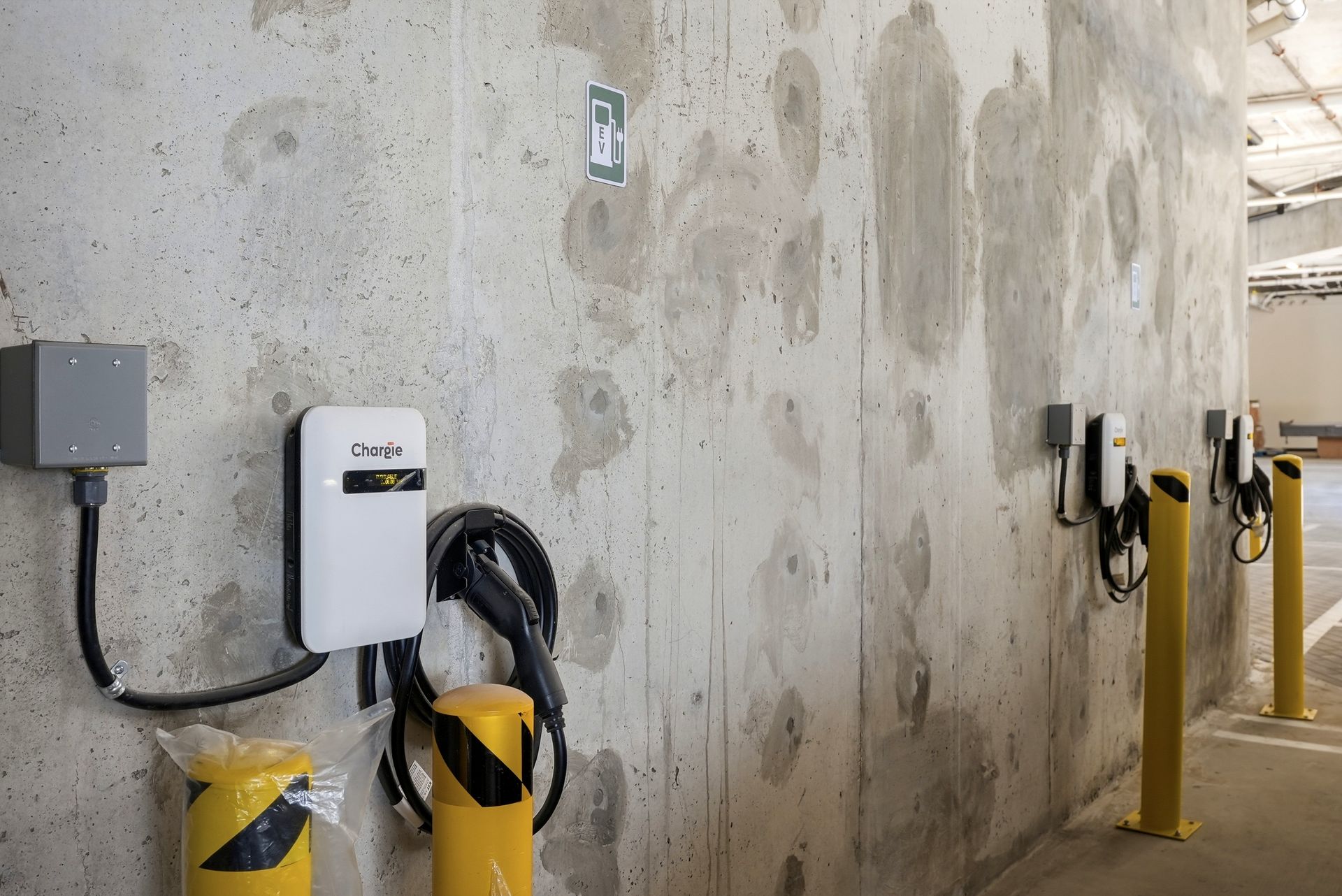 Concrete wall with electric vehicle charging stations and yellow protective bollards in a parking area
