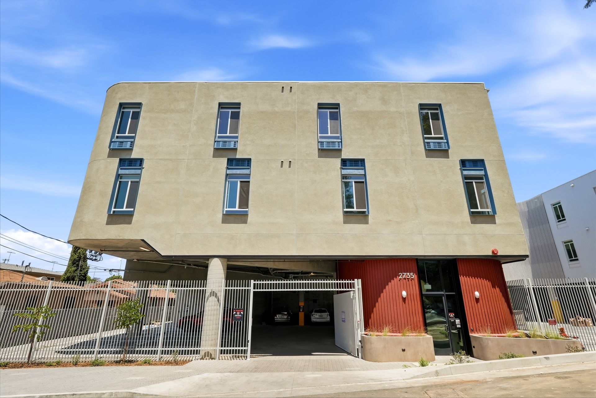 Modern beige building elevated on concrete pillars, with a garage and red doors below under a blue sky