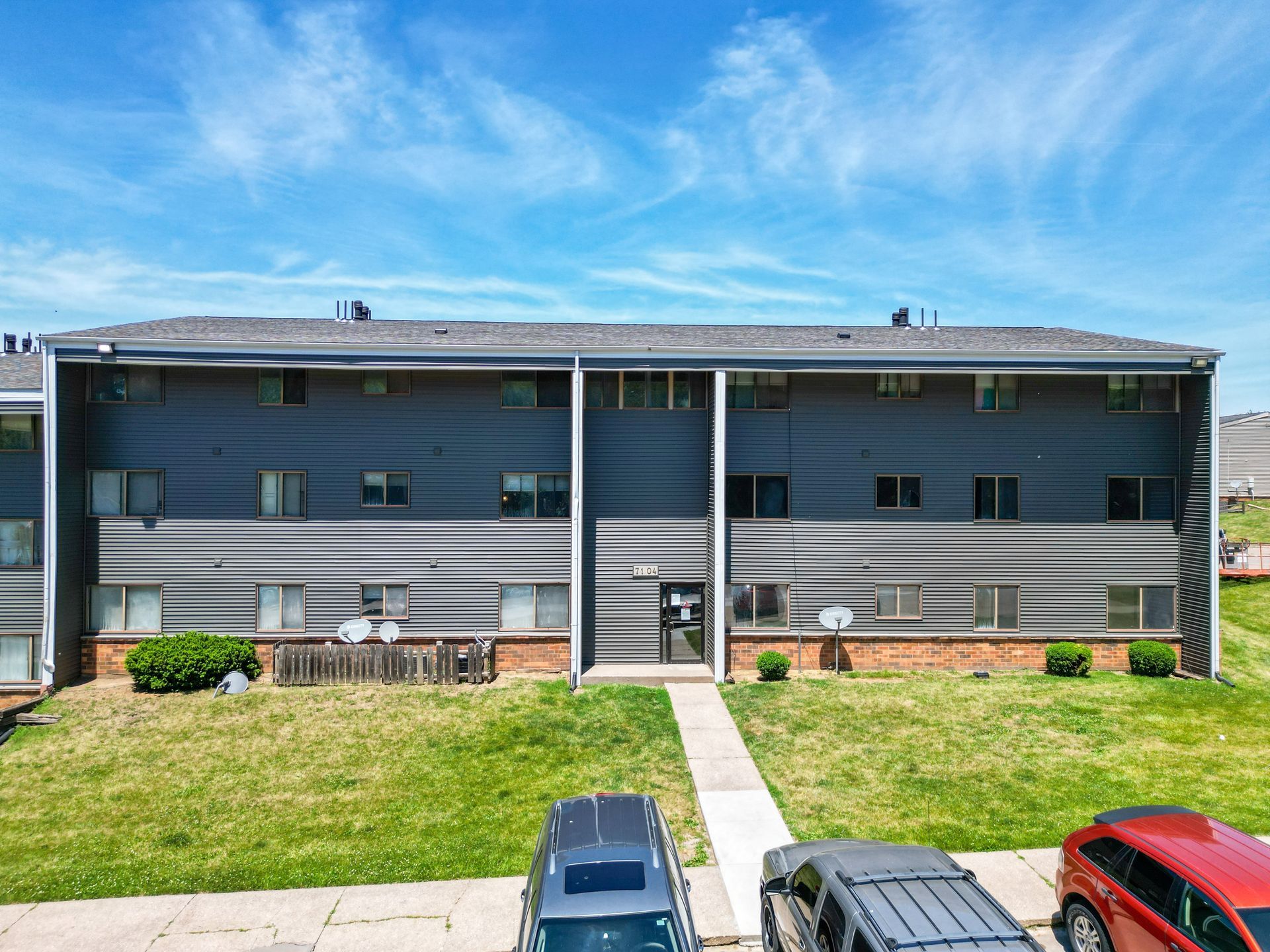 A row of cars are parked in front of a large apartment building.