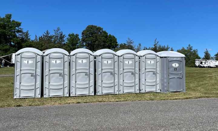 A row of portable toilets are lined up in a field.