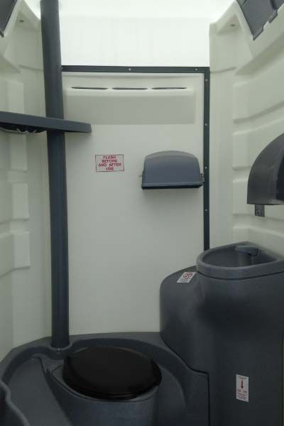 The inside of a portable toilet with a toilet and a trash can.