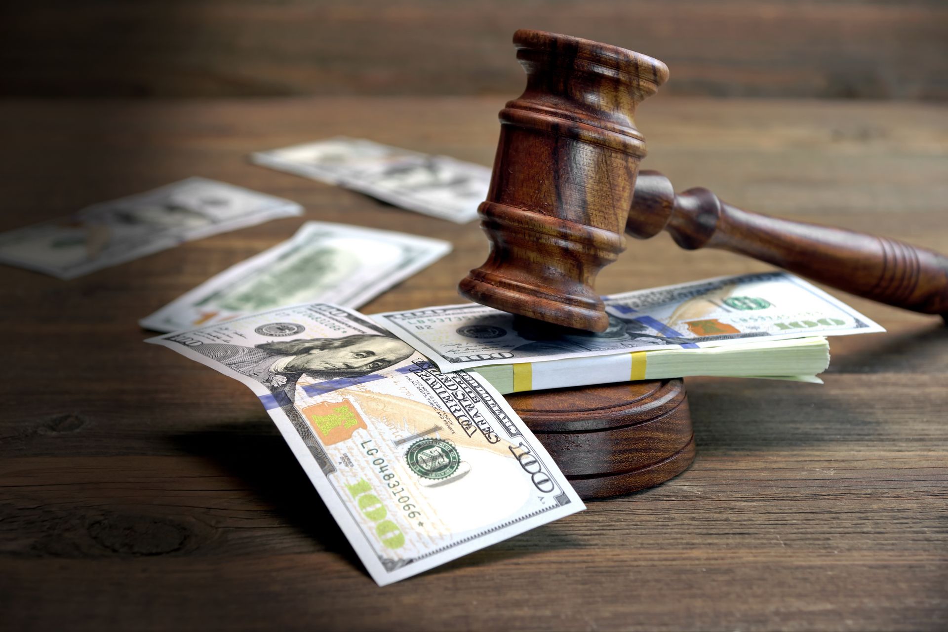 A wooden judge 's gavel is sitting on top of a pile of money on a wooden table.