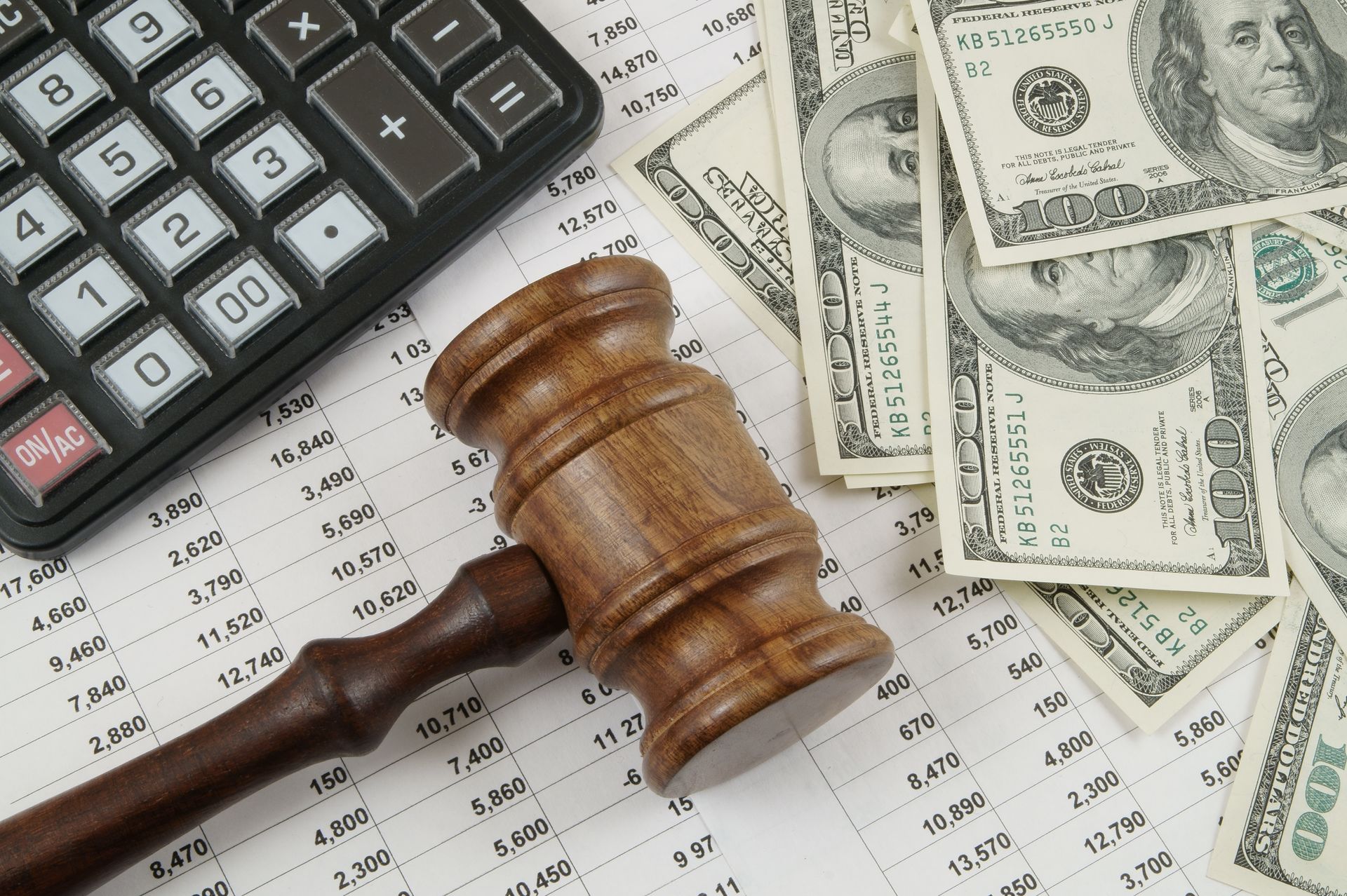 A wooden judge 's gavel sits on top of a pile of money next to a calculator