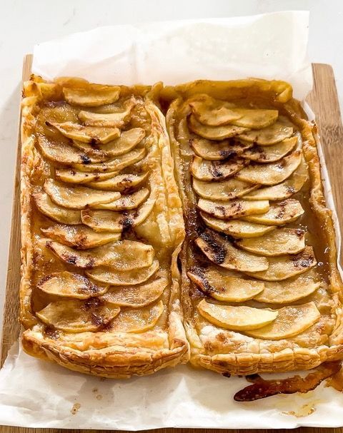 Two apple tarts are sitting on a wooden cutting board.