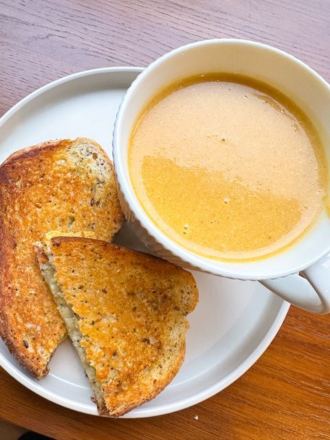 A cup of soup and two slices of grilled cheese on a plate