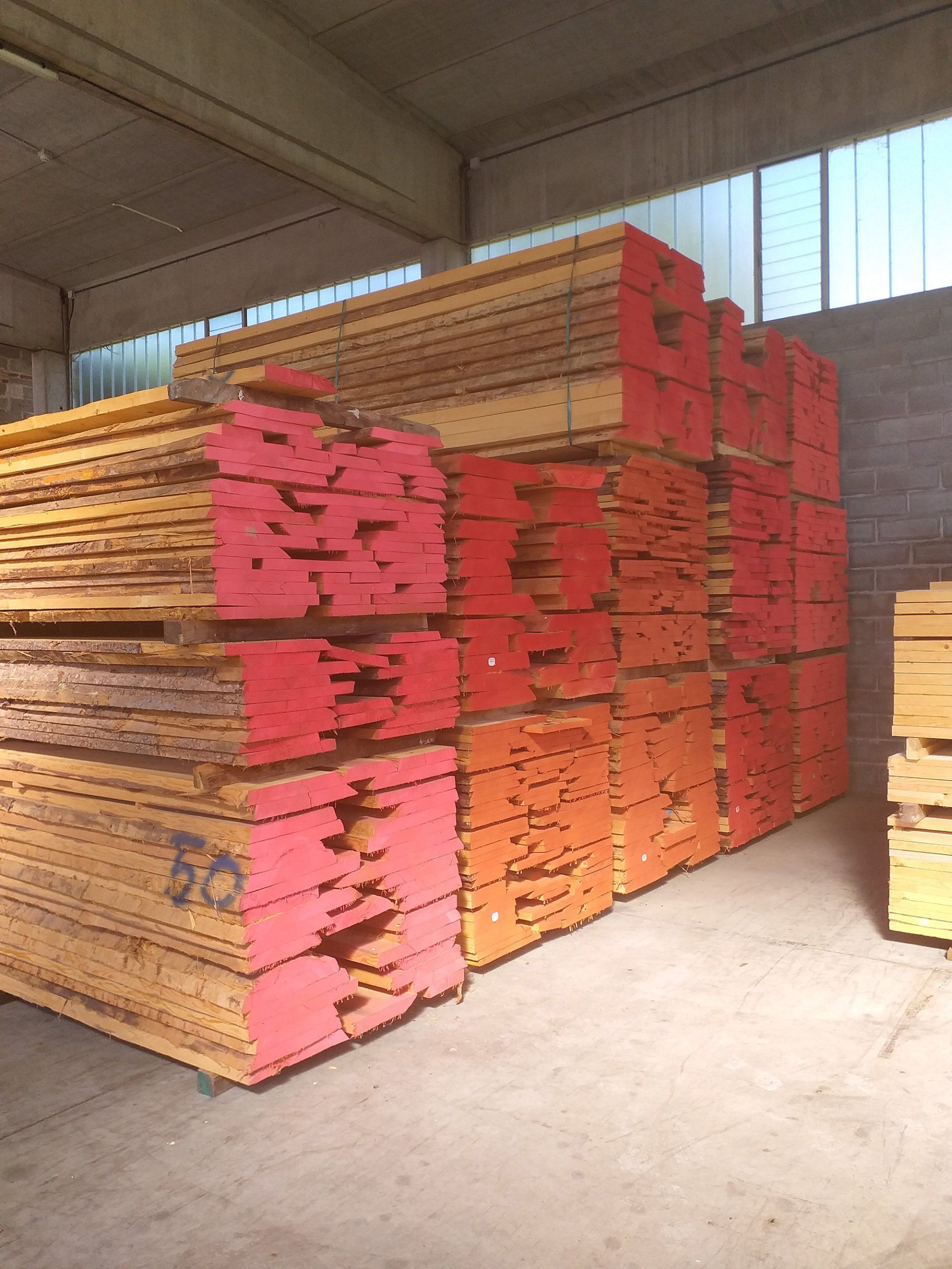 Pile di assi di legno arancioni e gialle, probabilmente materiali da costruzione, all'interno di un magazzino.