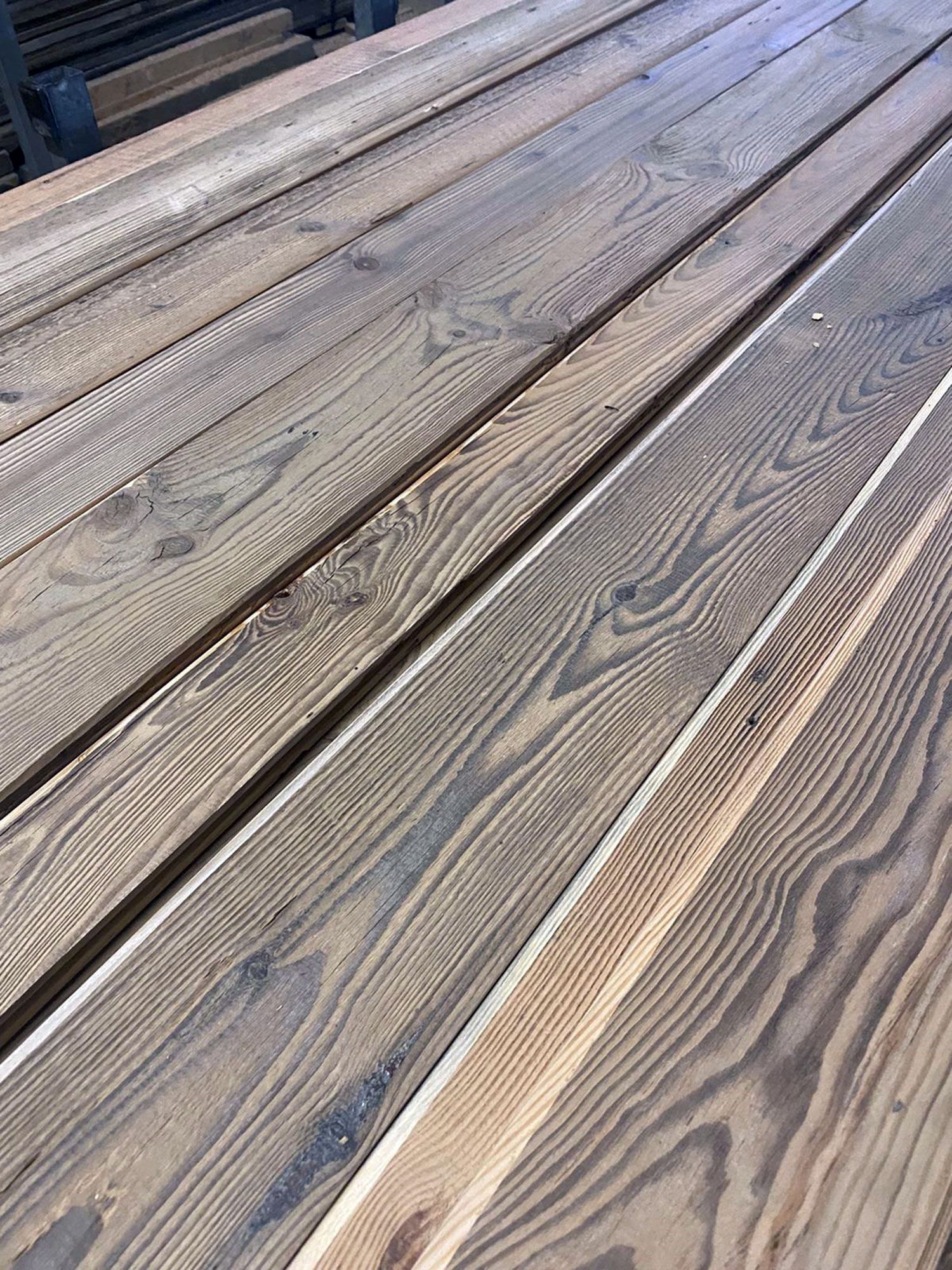 Tavole di legno impilate in diagonale, che mostrano le venature del legno e diverse sfumature di marrone e grigio.