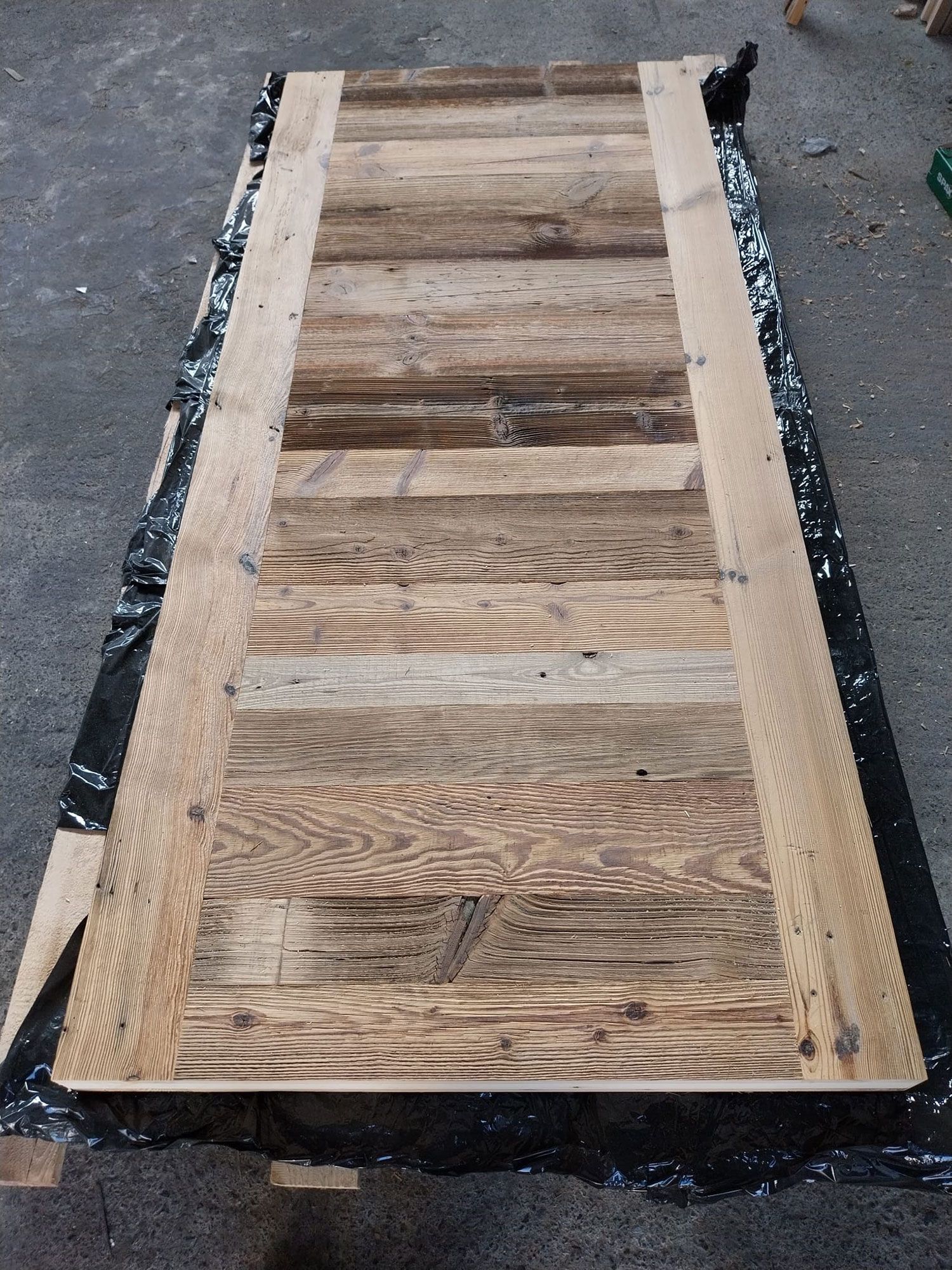 Porta di legno appoggiata su un lenzuolo nero. La porta è fatta di assi, dall'aspetto invecchiato.