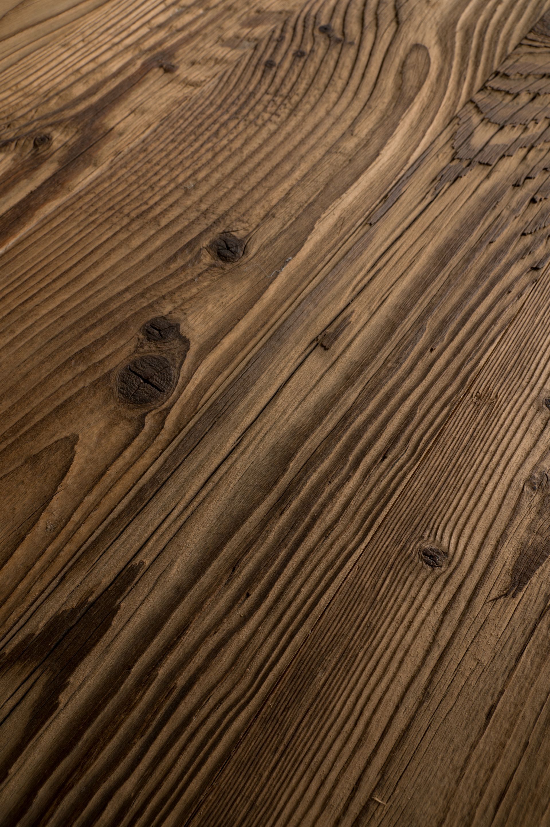 Primo piano di una superficie di legno stagionata con venature visibili, nodi e una calda tonalità marrone.