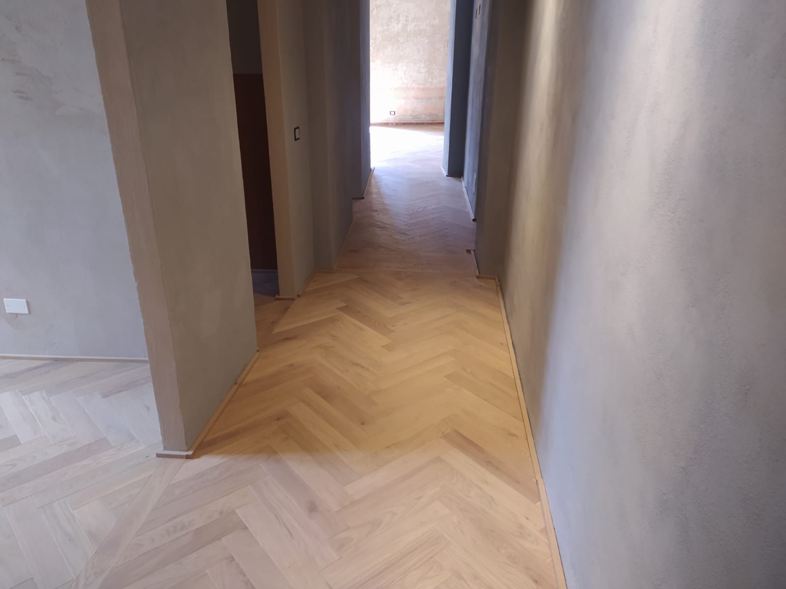 Pavimento in legno a spina di pesce in un corridoio con pareti grigio chiaro. 