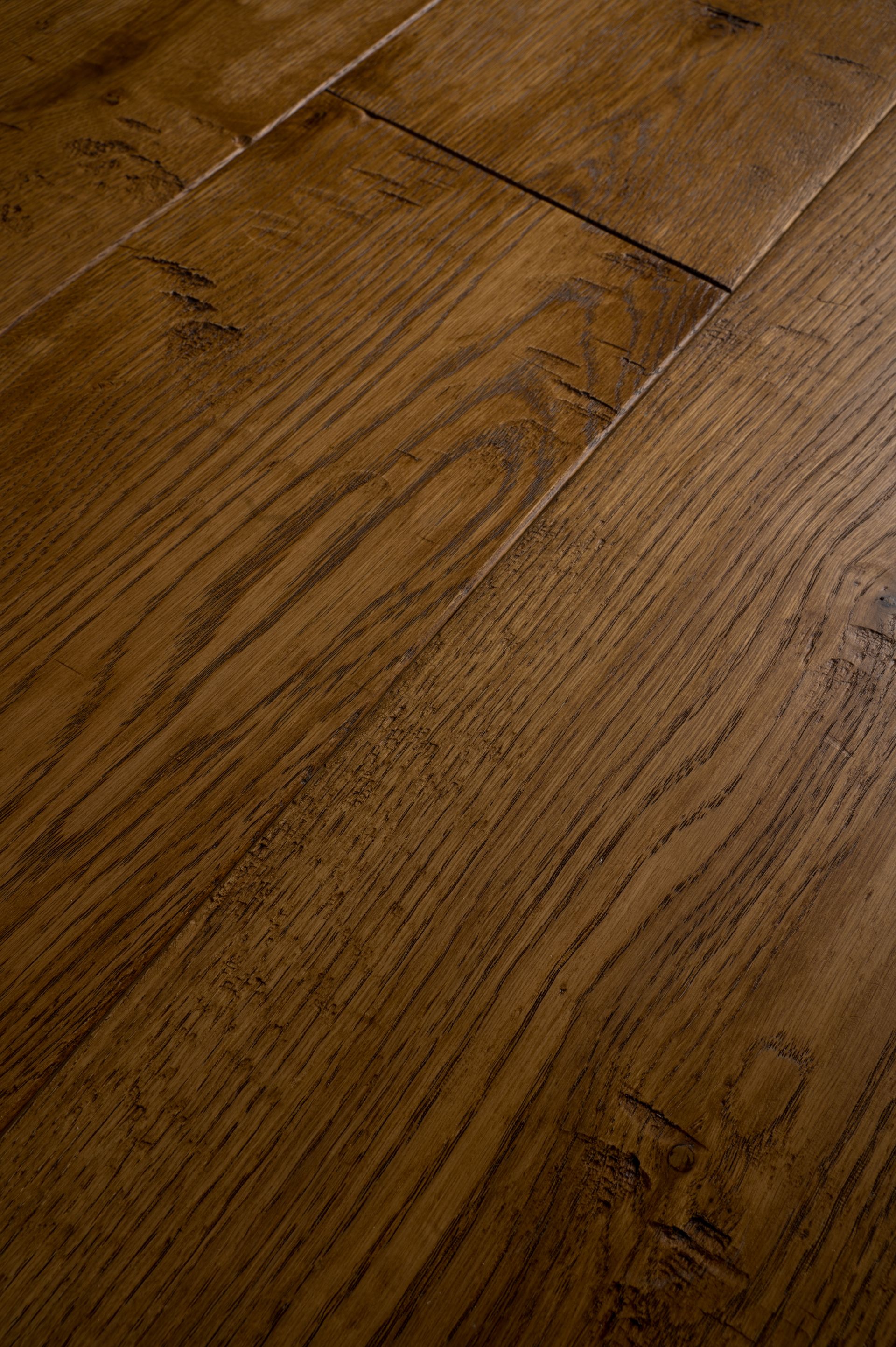 Primo piano del pavimento in legno massello marrone scuro, che mostra le venature del legno e le scanalature tra le assi.