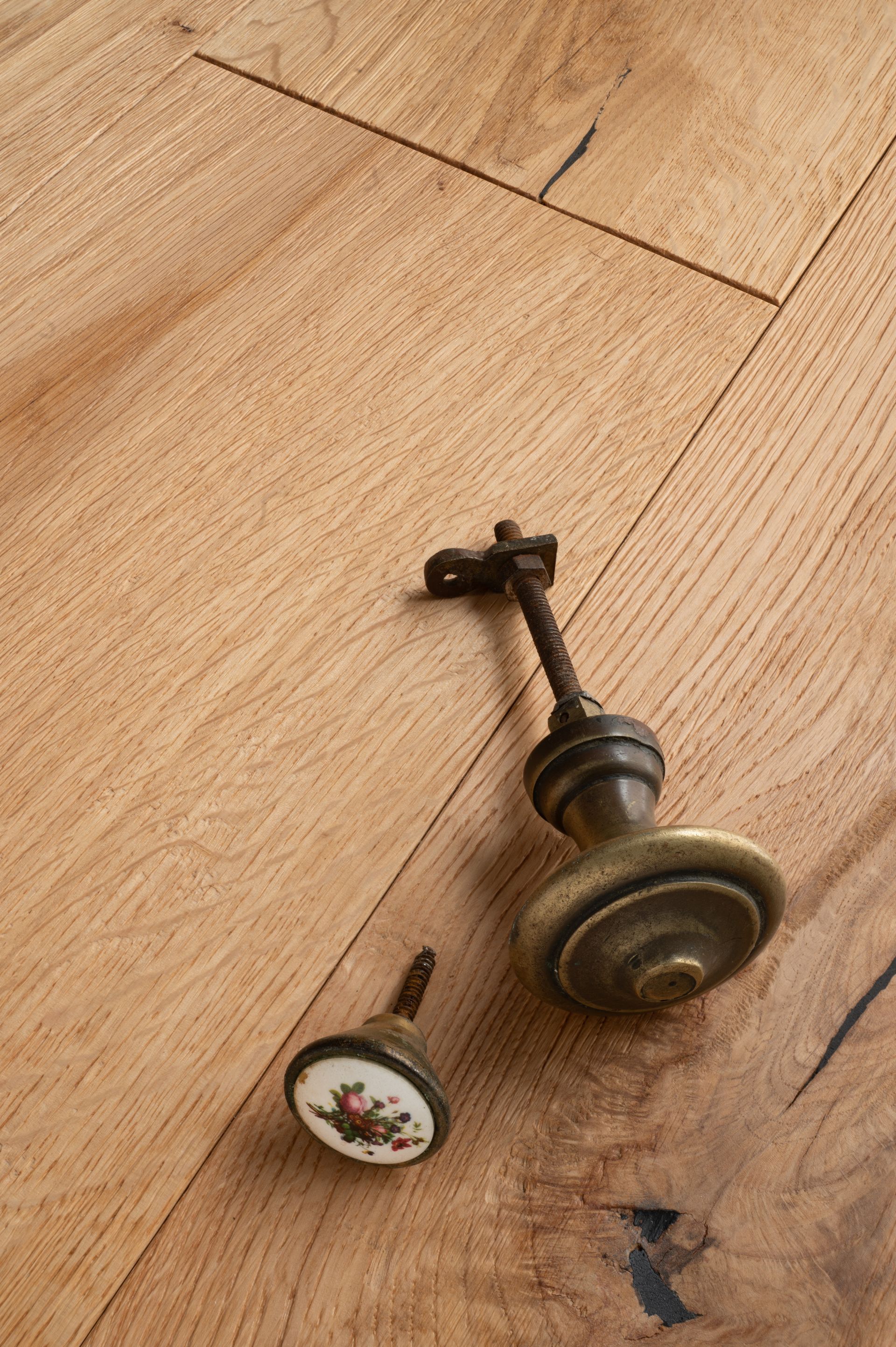 Due pomelli antichi su un pavimento in legno chiaro; uno con un motivo floreale, l'altro con un grande pomello in ottone.