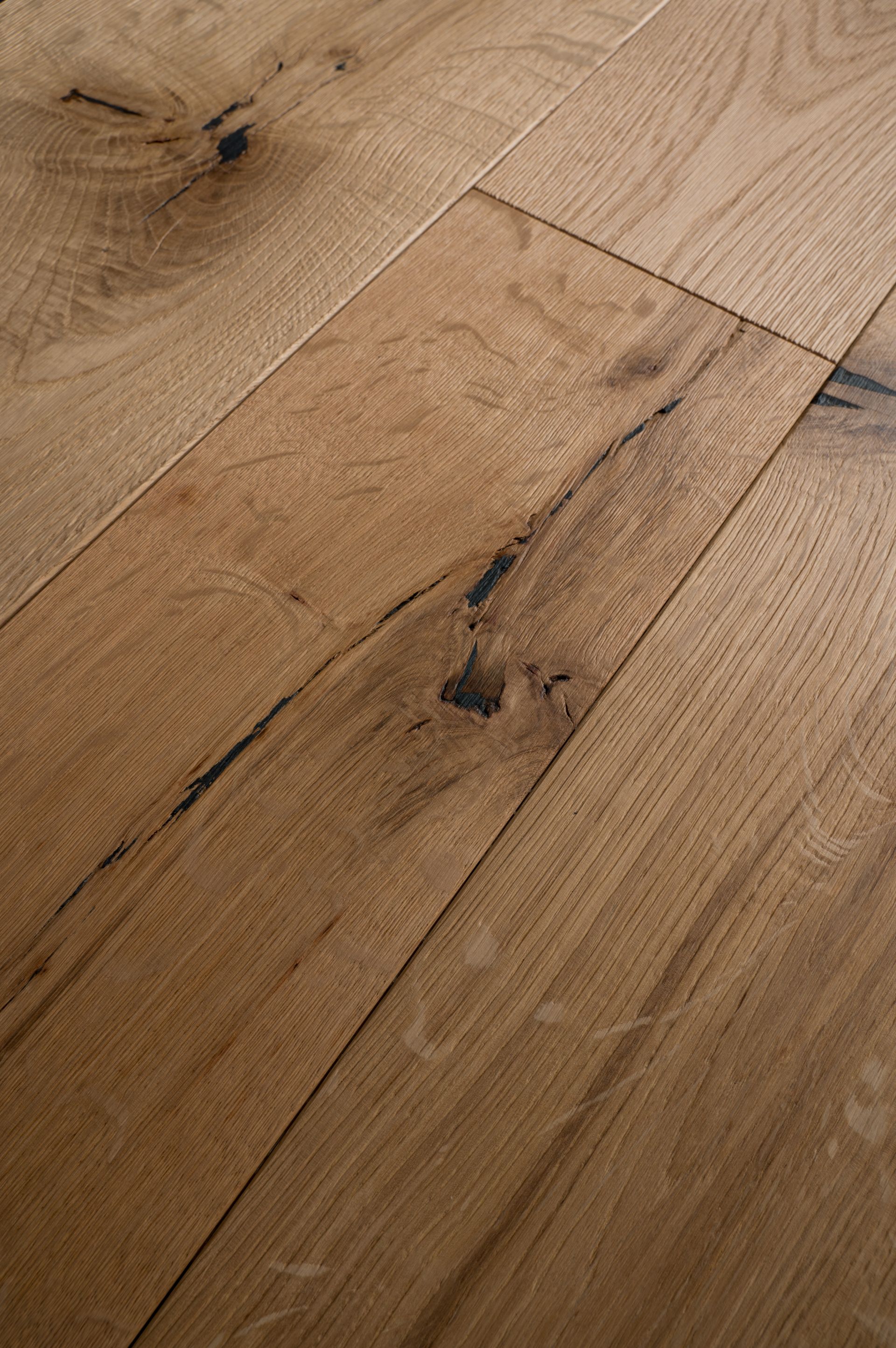 Pavimento in legno con diverse tonalità di marrone e scuro, nodi irregolari. Le assi sono posate orizzontalmente, con la luce che si riflette sulla superficie.