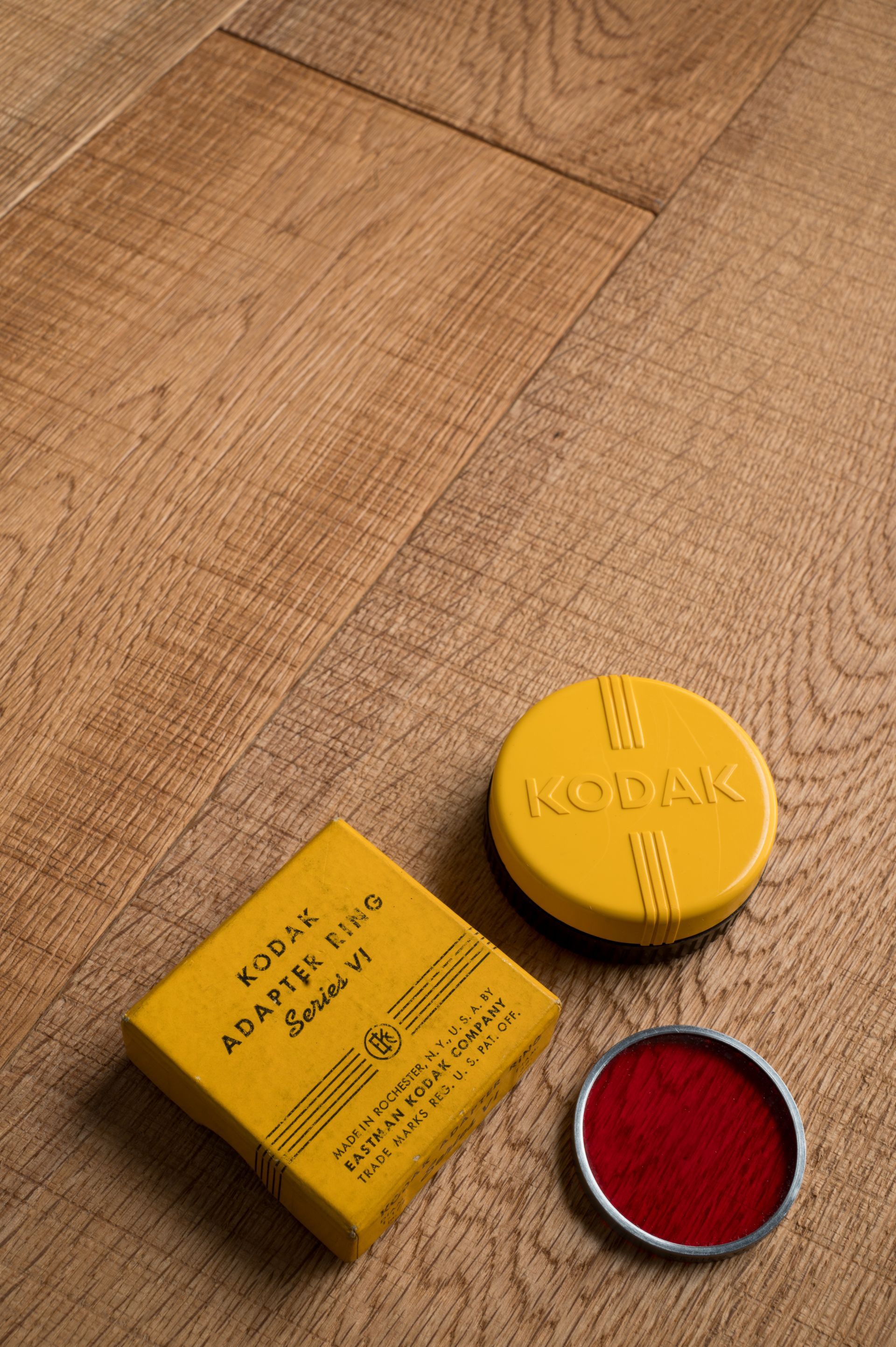 Scatola di pellicola Kodak gialla, contenitore per pellicola e filtro rosso su una superficie di legno.