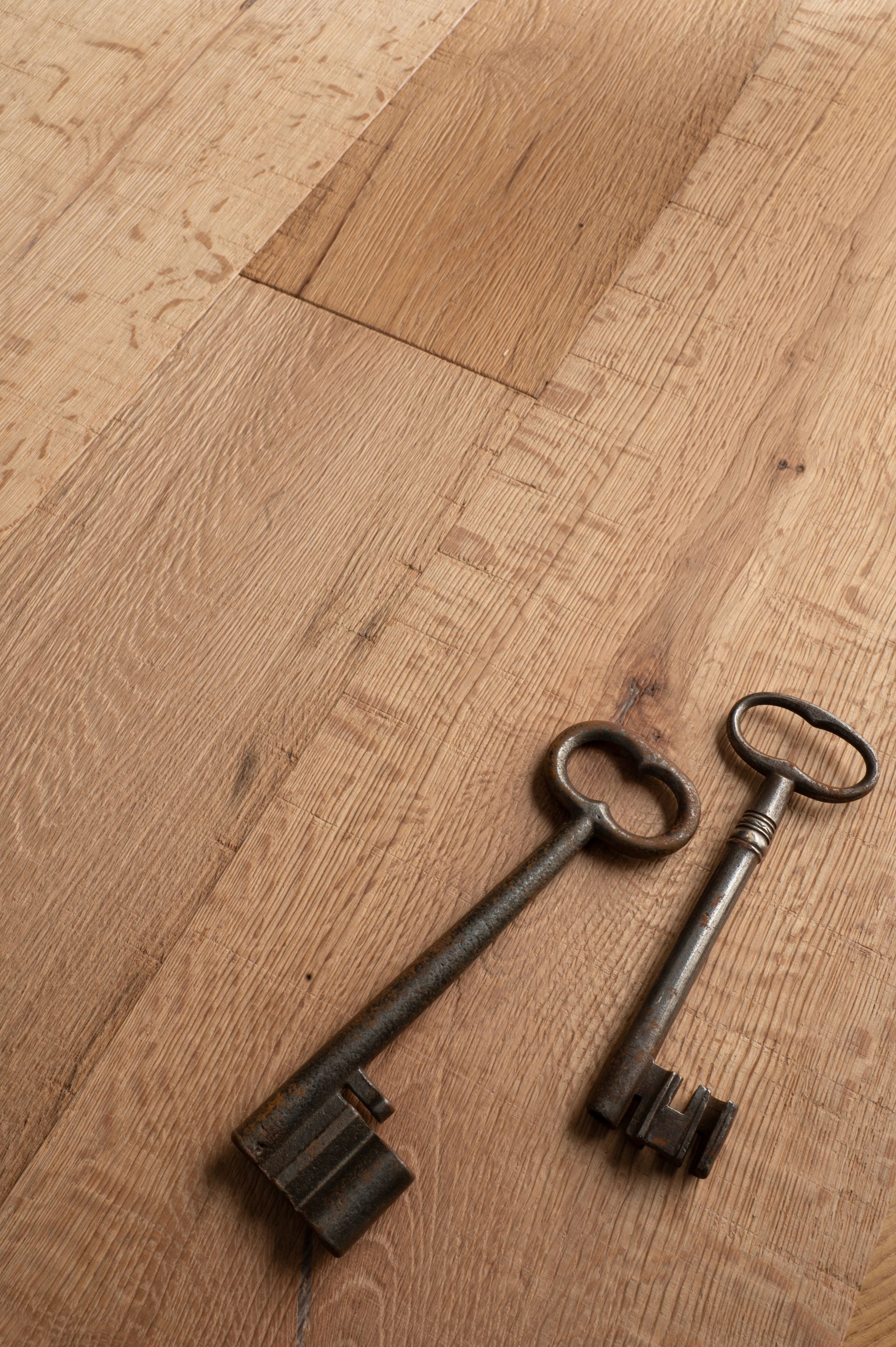 Due chiavi antiche su una superficie di legno marrone chiaro. Una chiave presenta dettagli più intricati dell'altra.