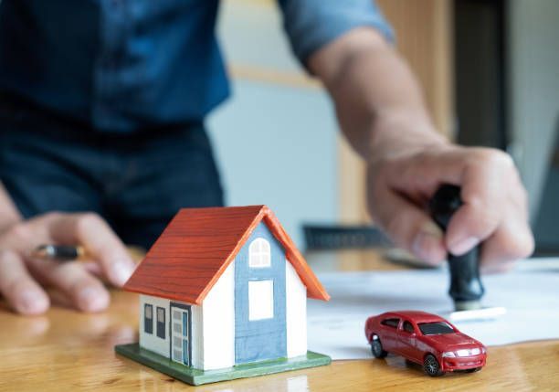 Person stamping a document next to a toy house and a red toy car on a table.
