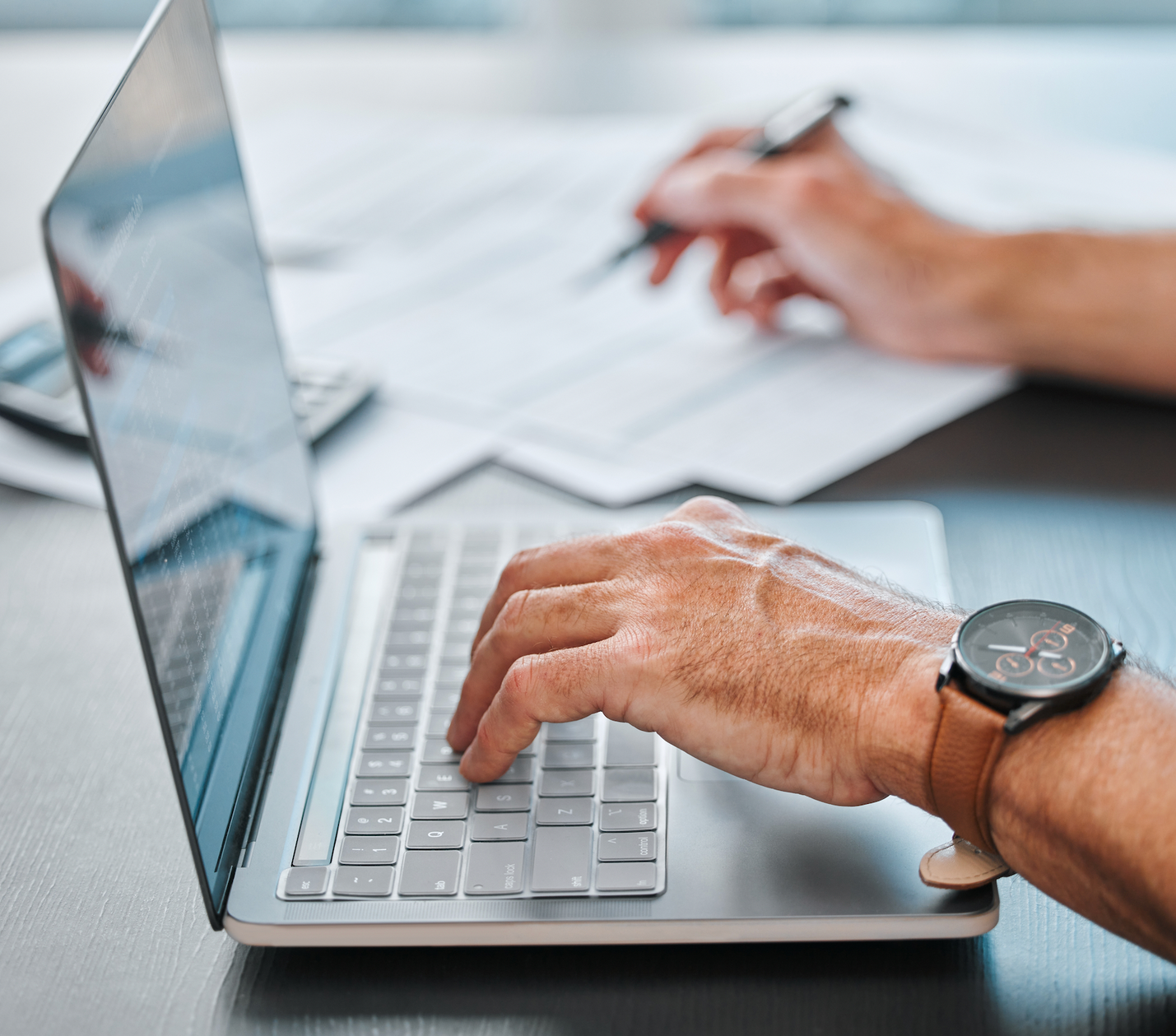 A man is sitting at a desk using a laptop and a tablet.