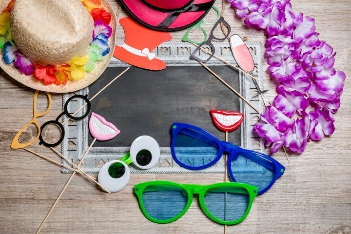 Colorful sunglasses and summer accessories arranged on a wooden surface with a straw hat and flower lei