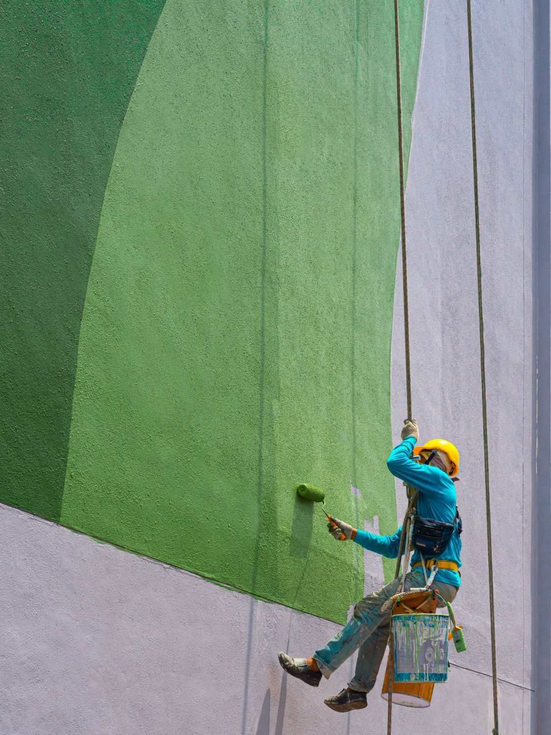 A man is hanging from a rope and painting a wall.