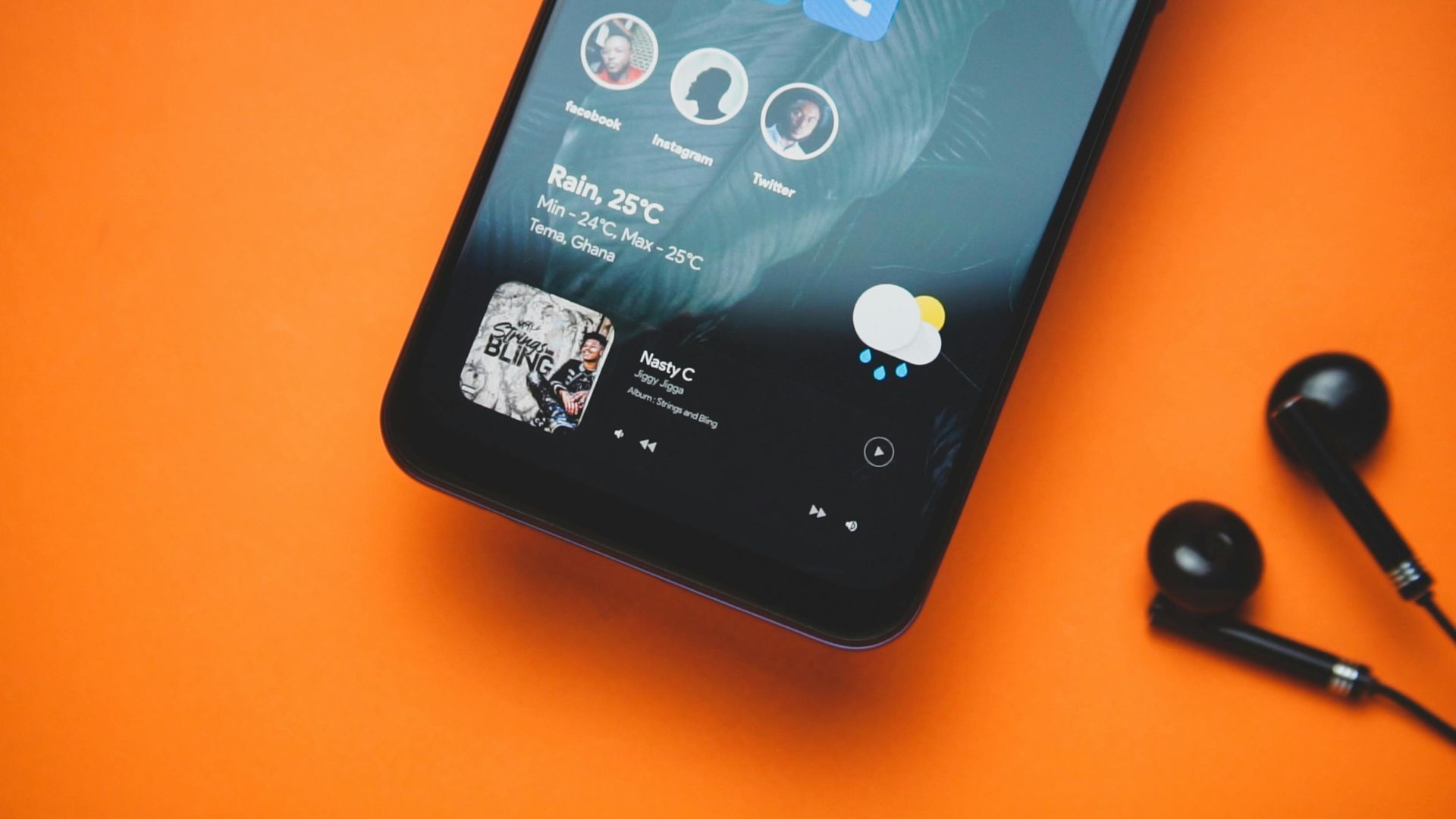 Black smartphone with a music player and earbuds on an orange surface.