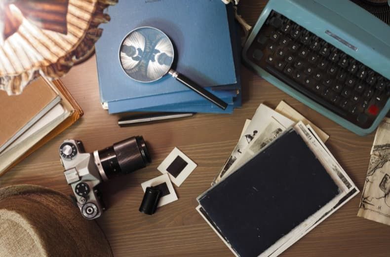 a desk with a typewriter , camera , magnifying glass , and other items for investigations.