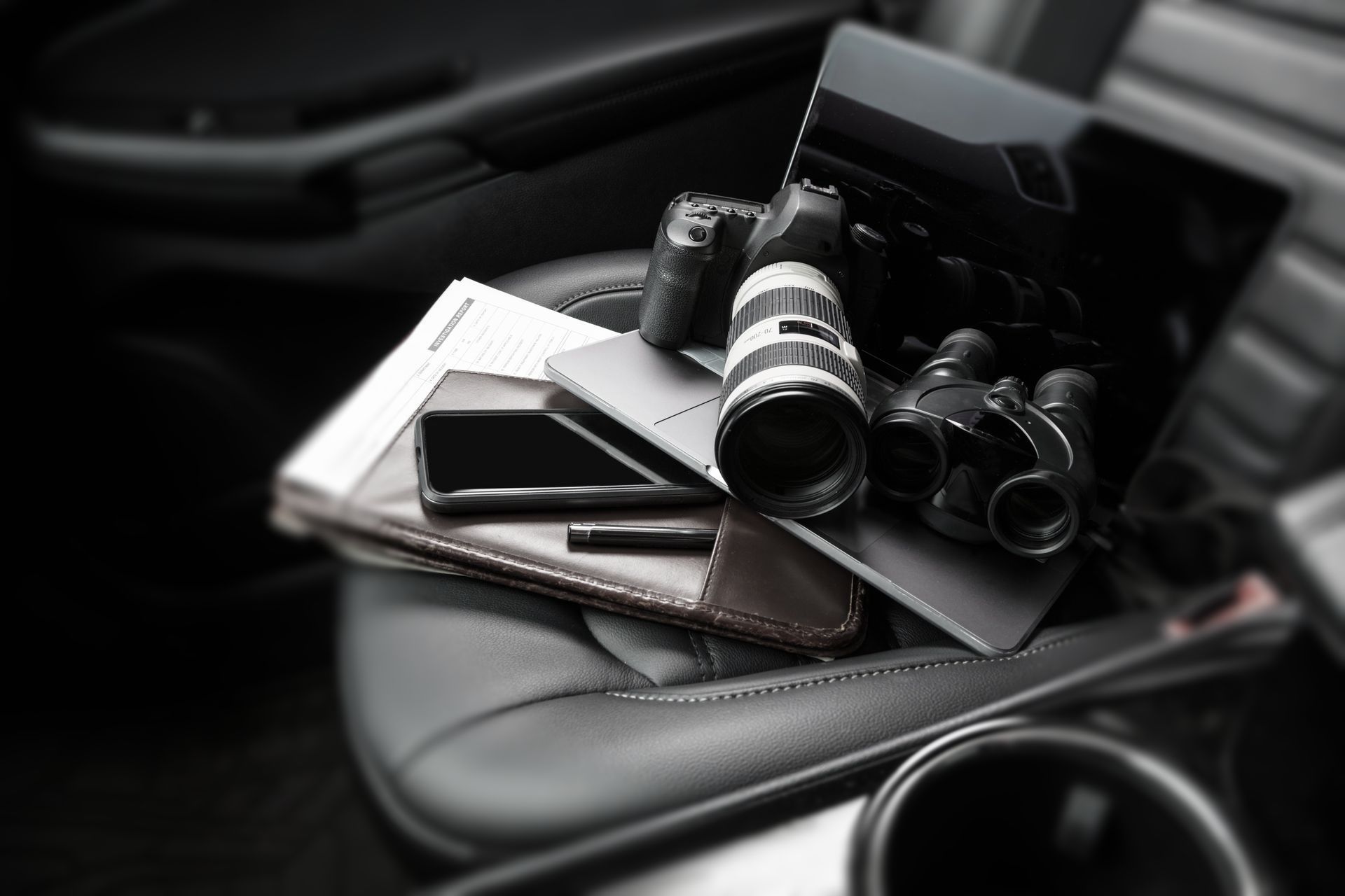 PI equipment like a camera, laptop, phone and binoculars on a car seat