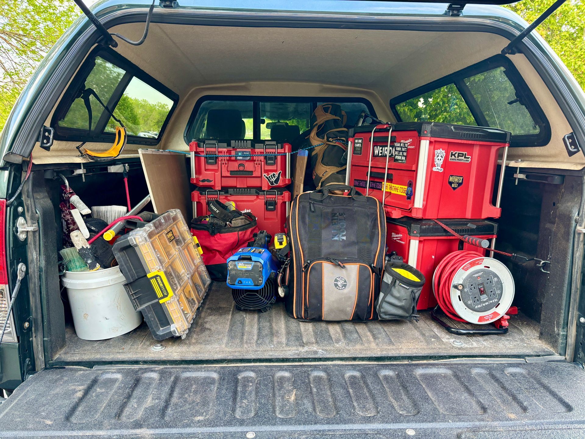 Truck bed filled with tools in various containers, including red toolboxes and a coiled extension cord.