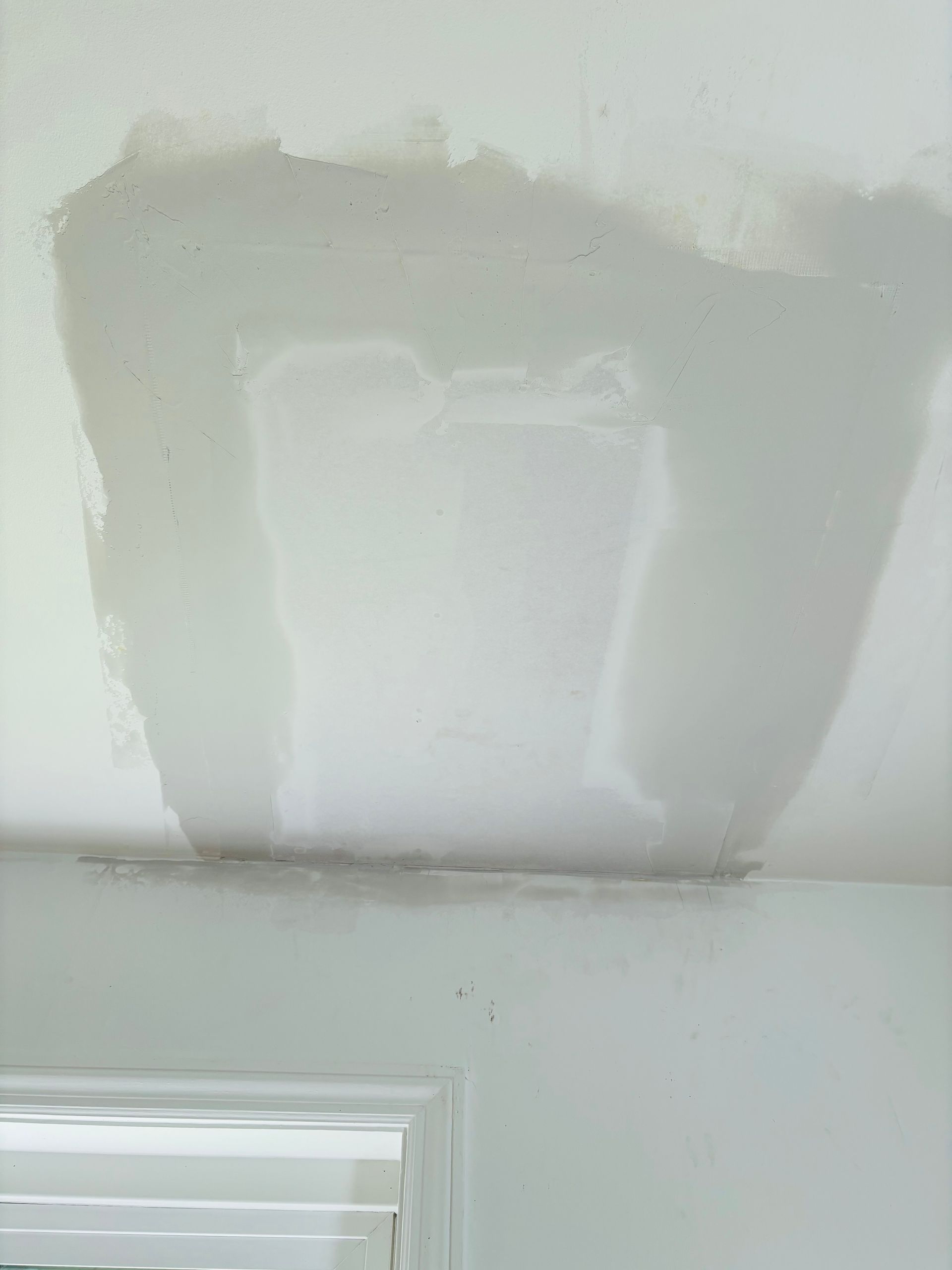 Ceiling damage showing water stains and repair work in a white room.