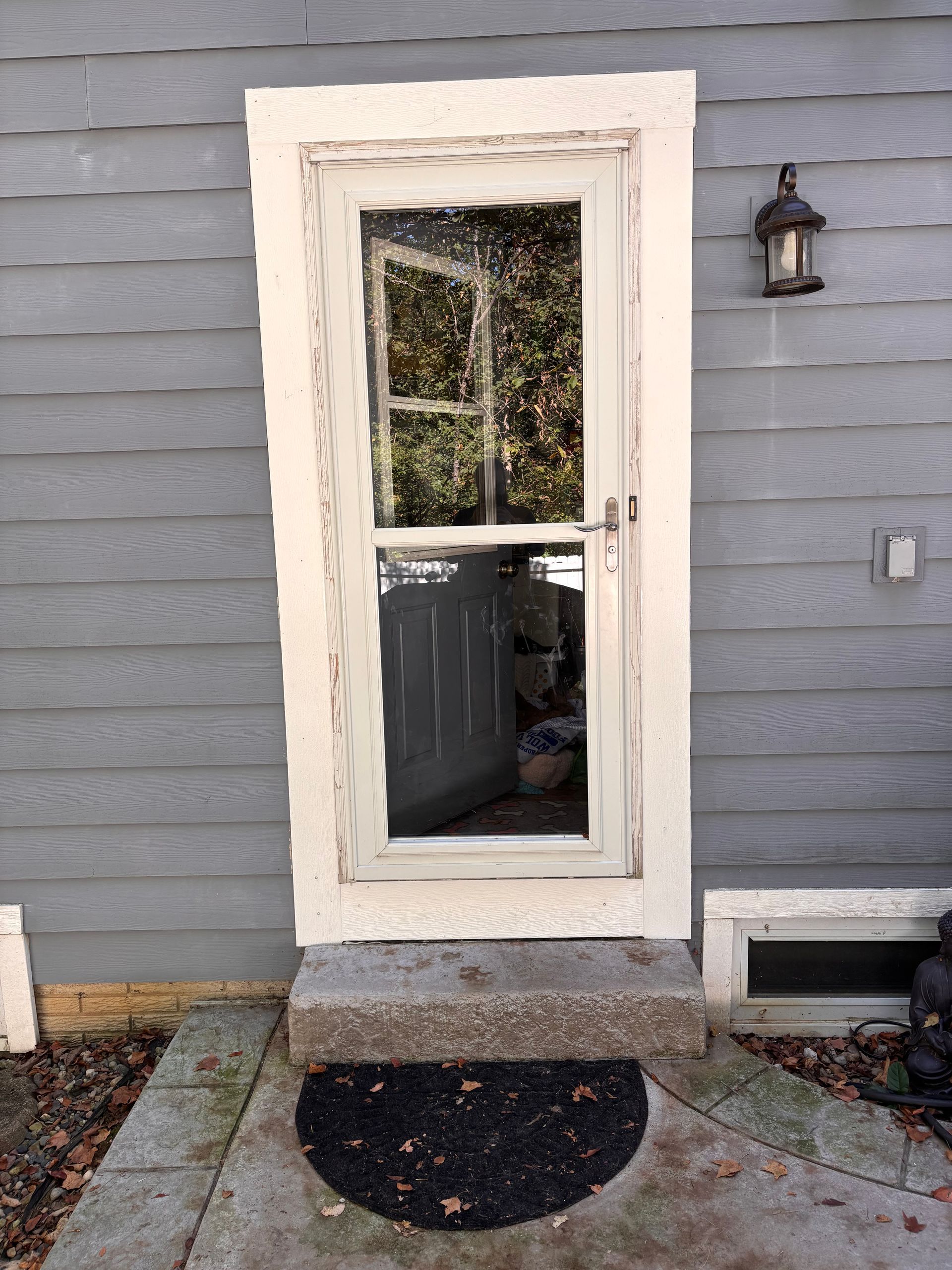 White screen door with distressed frame, gray siding background, stone step.