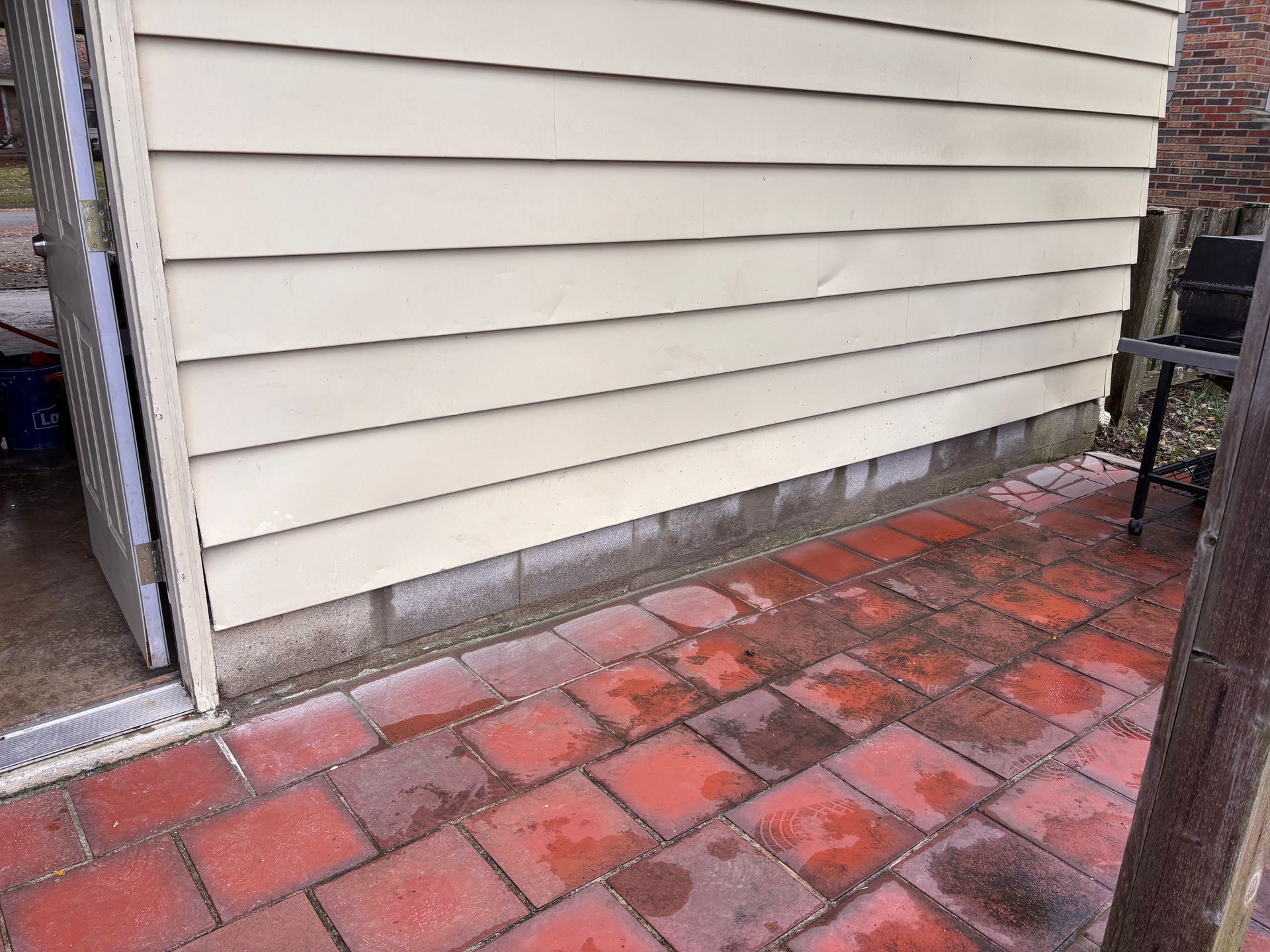 Red brick patio next to a beige siding wall; outdoor setting.