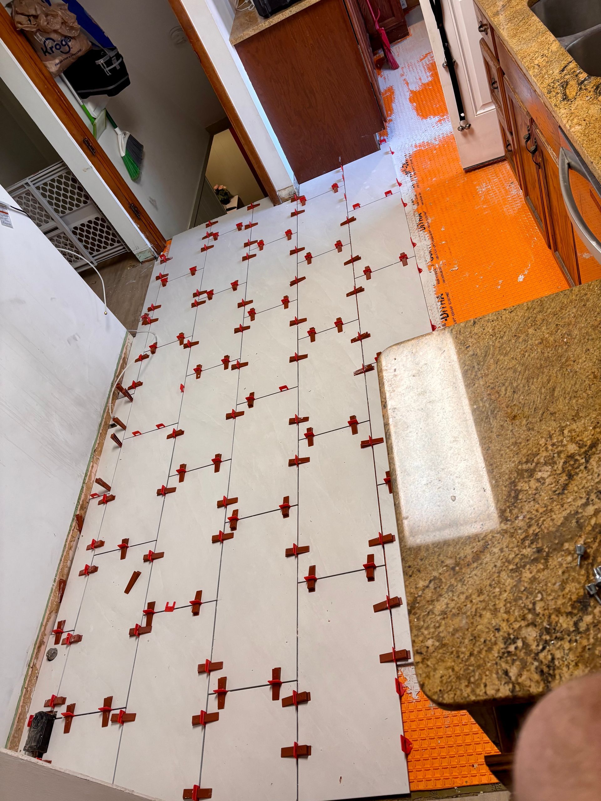White floor tiles with red spacers are being installed, near a counter.