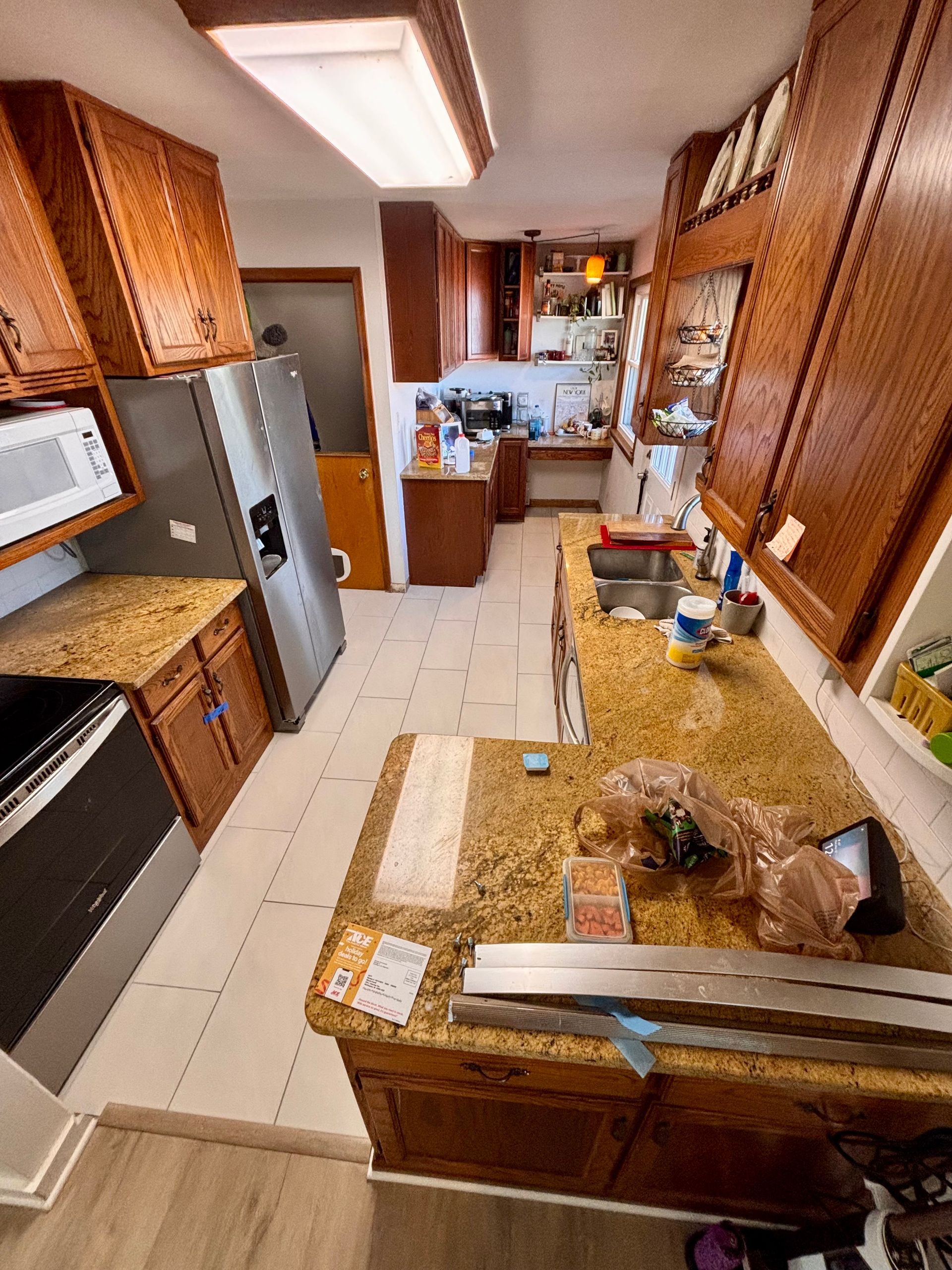 Narrow kitchen with granite countertops, wooden cabinets, stainless steel appliances, and a long fluorescent light.