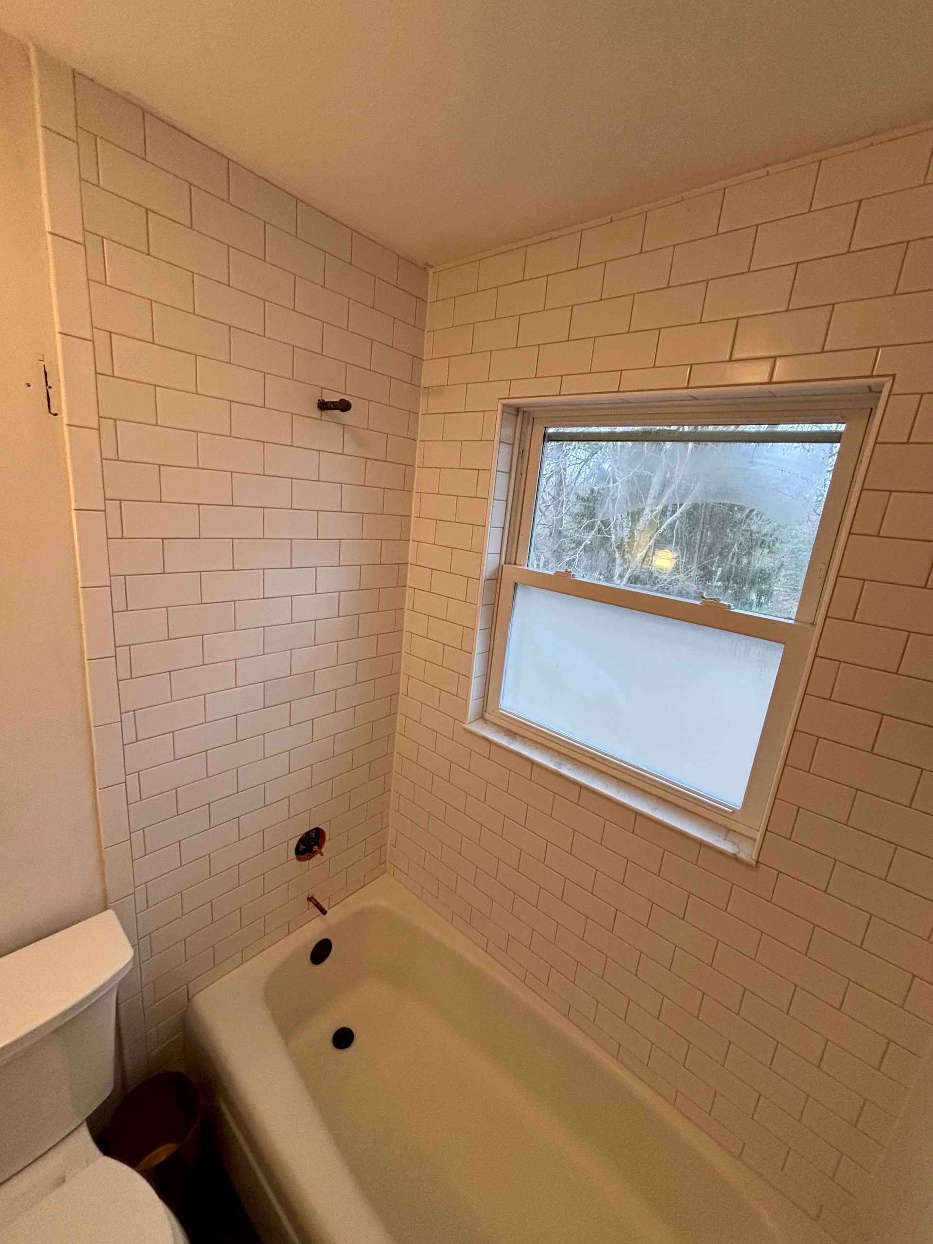 Bathroom with white tub, window, and patterned tile walls.